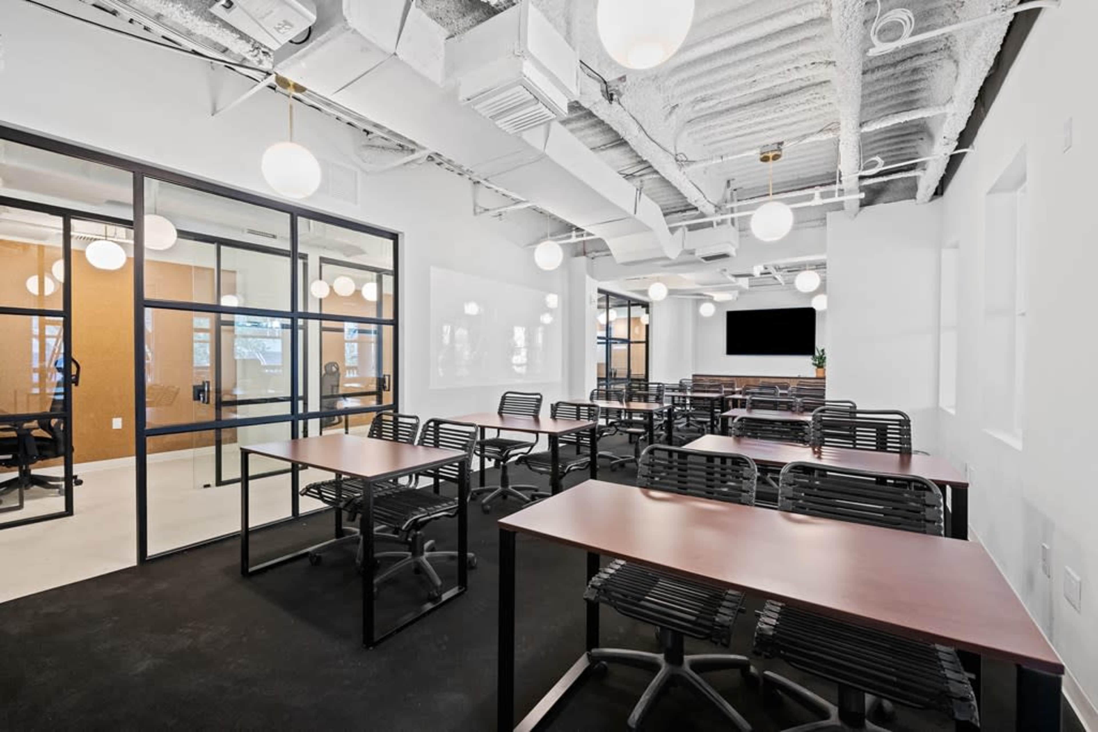A modern office space with several black chairs and wooden tables arranged in a layout suitable for meetings or collaborative work.