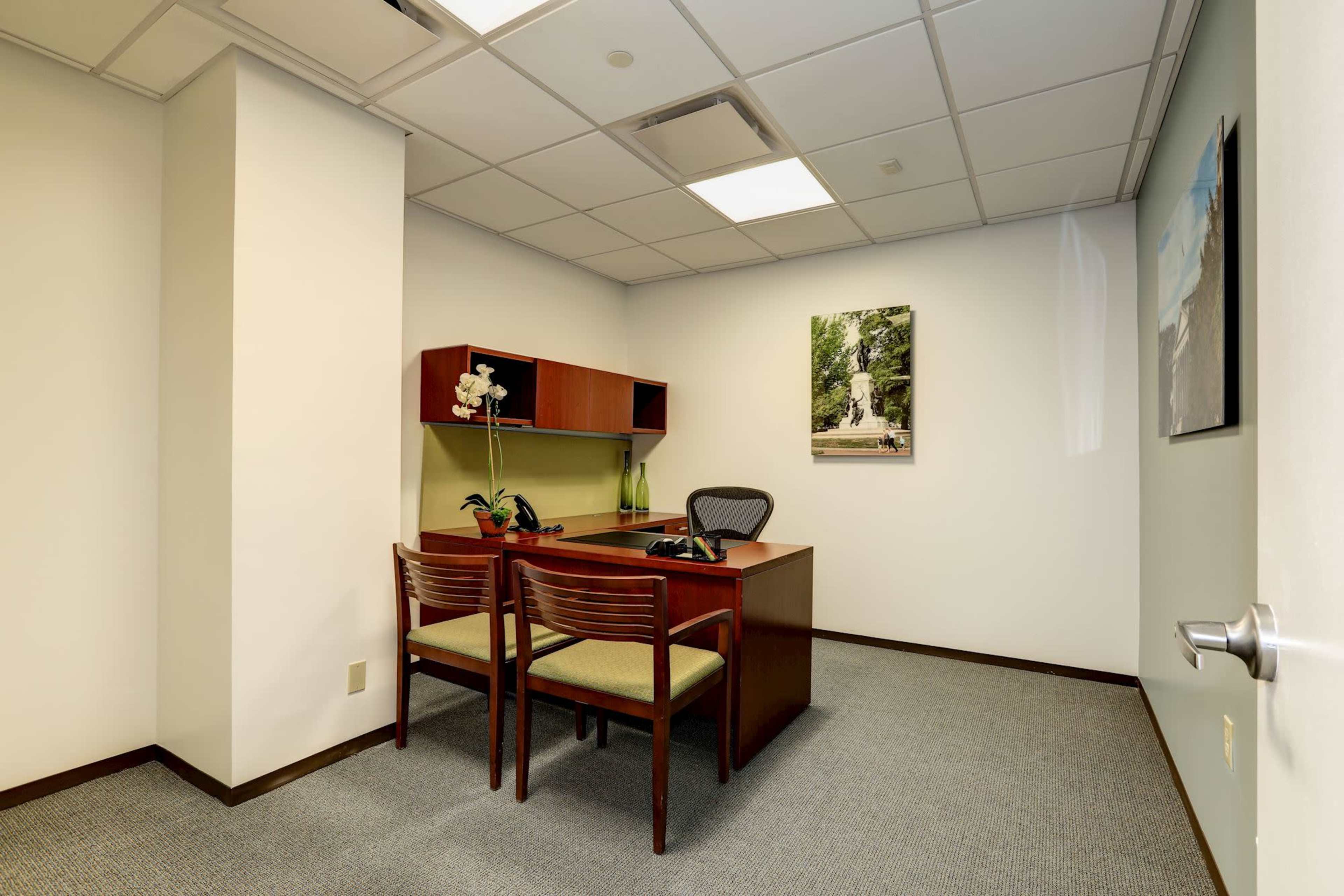 A small, modern office with a desk, two chairs, and a wall-mounted artwork.