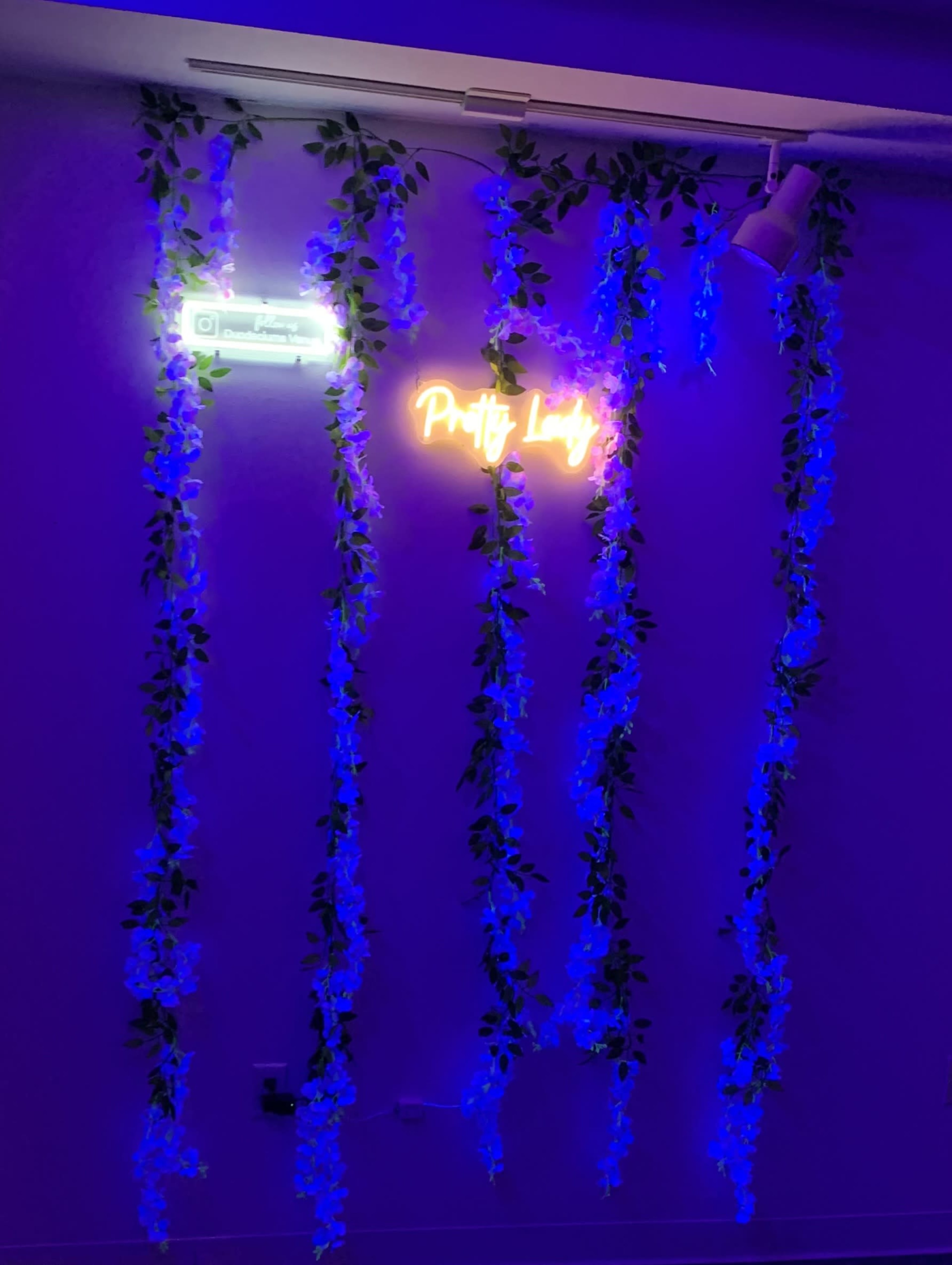 A wall adorned with blue LED lights and hanging floral decorations features a neon sign that reads "Pretty Lady."
