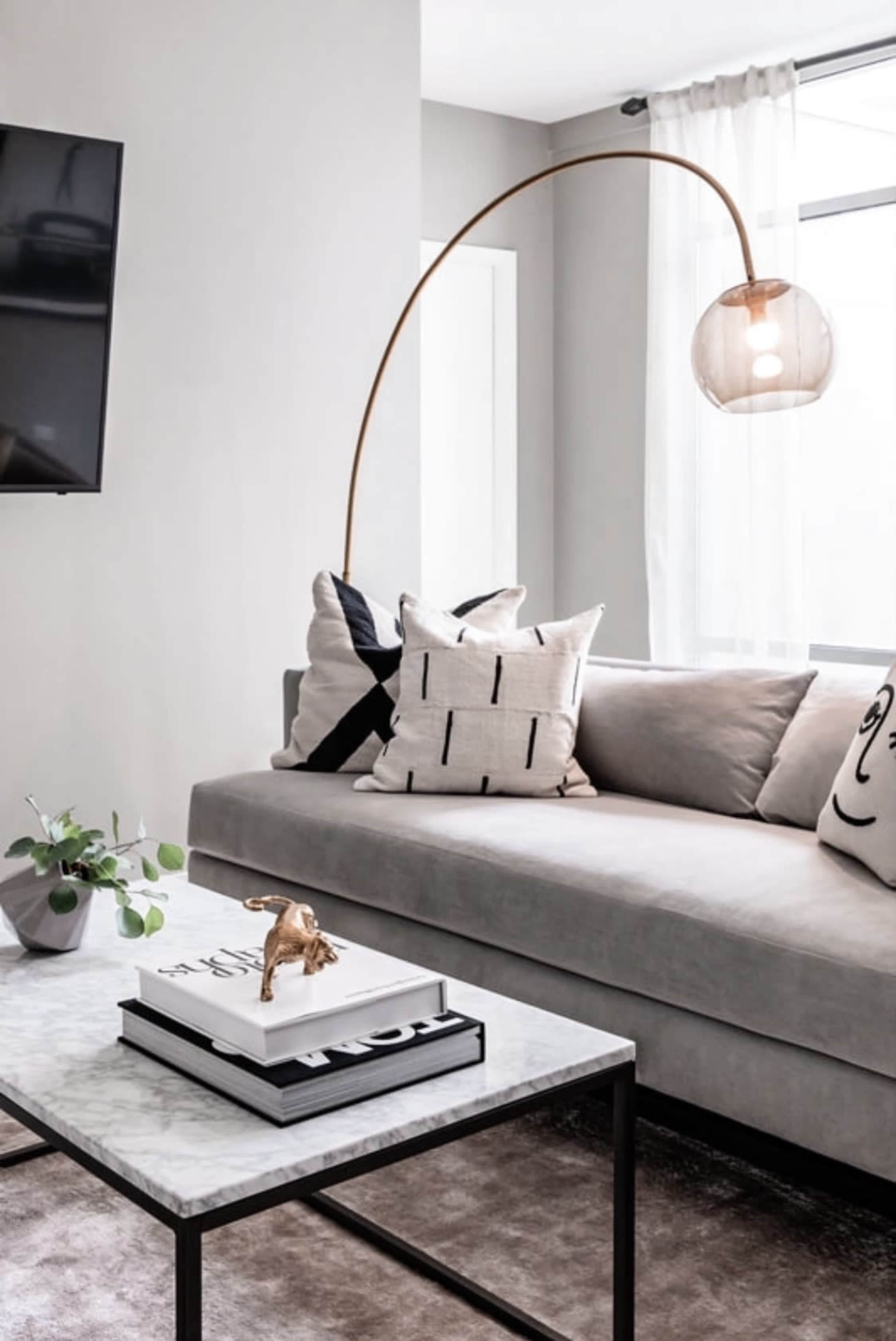 The living room features a light gray sofa with patterned cushions, a marble coffee table, and a modern arc floor lamp.