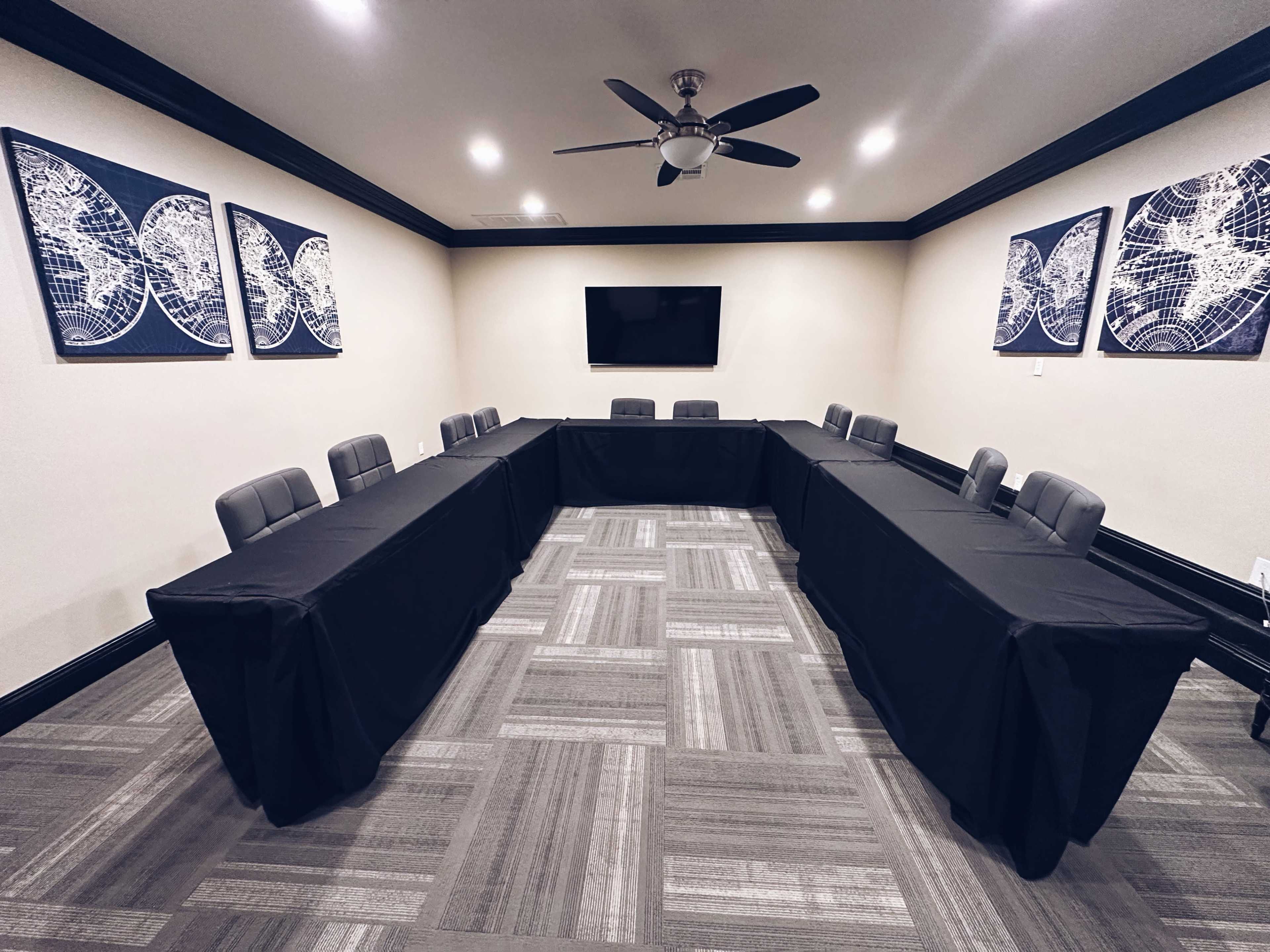 A conference room arranged with two sets of tables facing each other, black tablecloths covering the tables, and maps displayed on the walls.