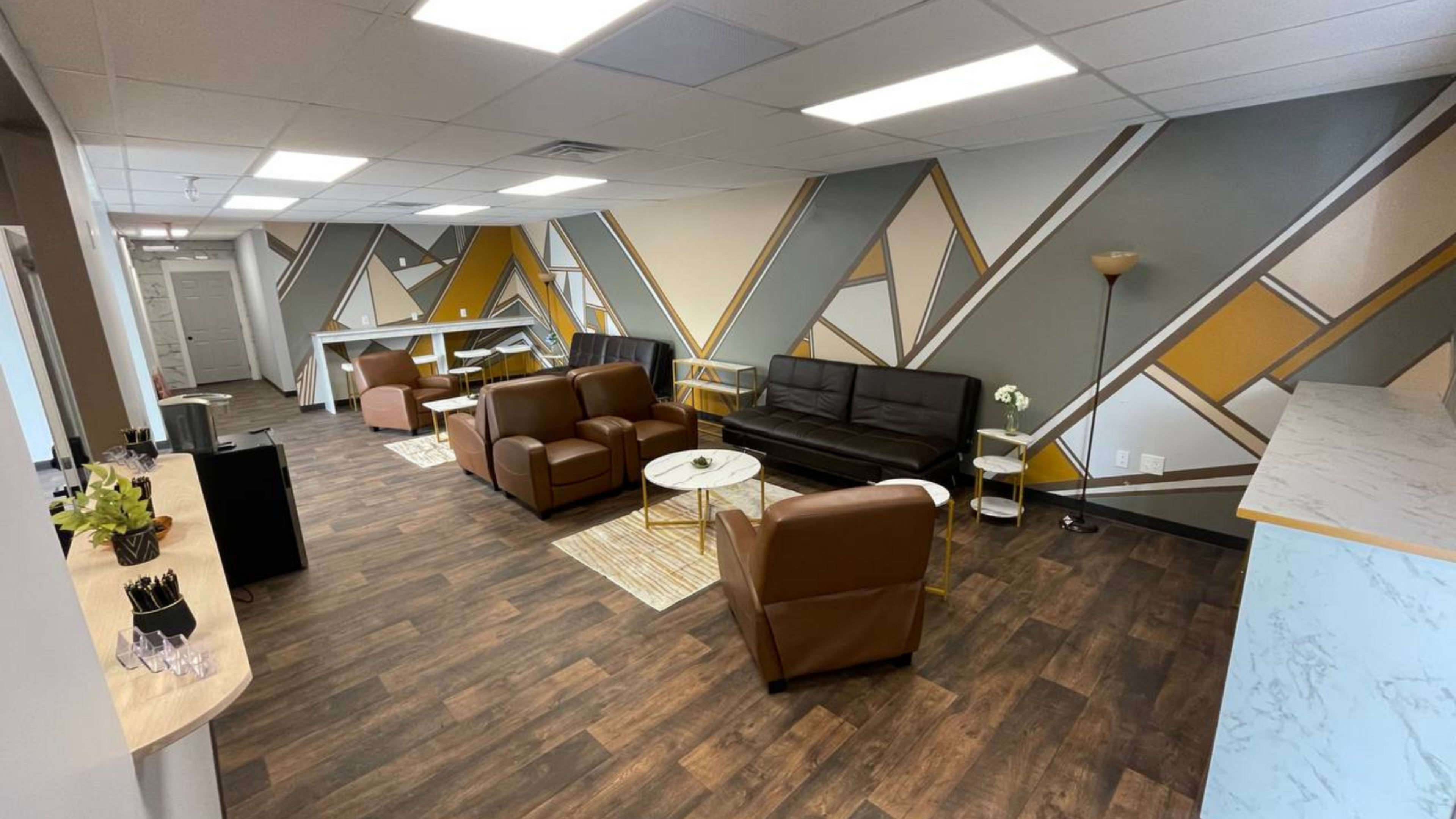 The image shows a modern office lounge area with four seating arrangements, a coffee table, and a decorative wall featuring geometric patterns in gray, yellow, and white.