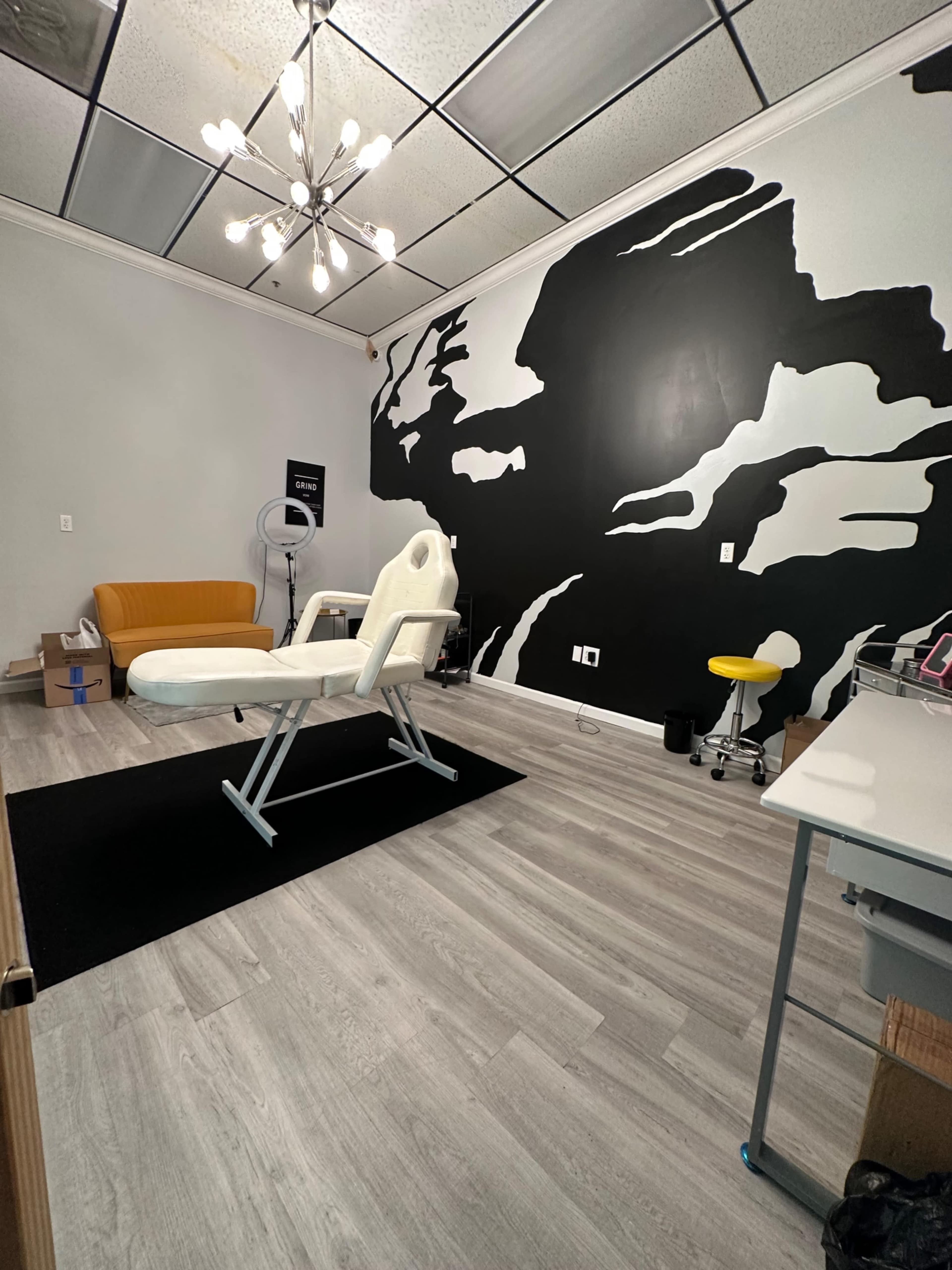 A well-lit treatment room featuring a white adjustable chair, a black-and-white mural on one wall, and various furniture and equipment arranged throughout the space.