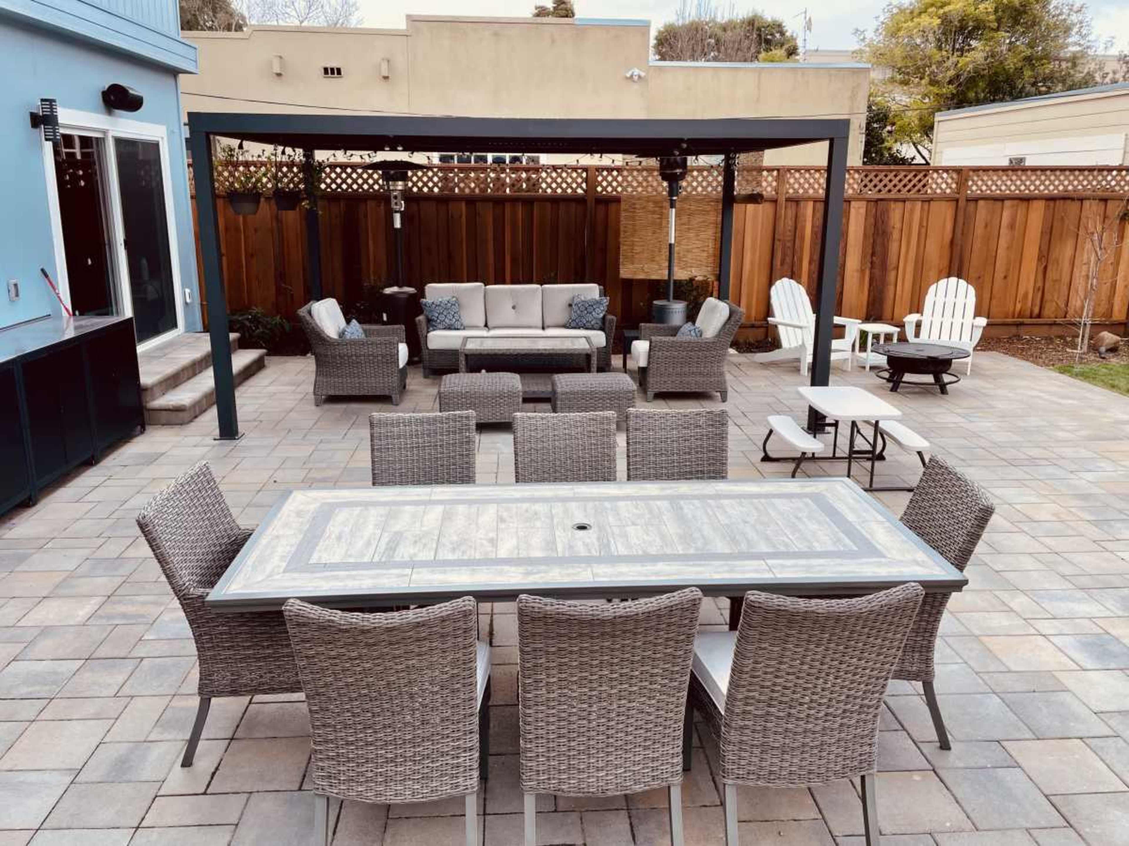The outdoor patio features a large dining table surrounded by wicker chairs, with a sectional sofa and several lounge chairs arranged underneath a canopy.