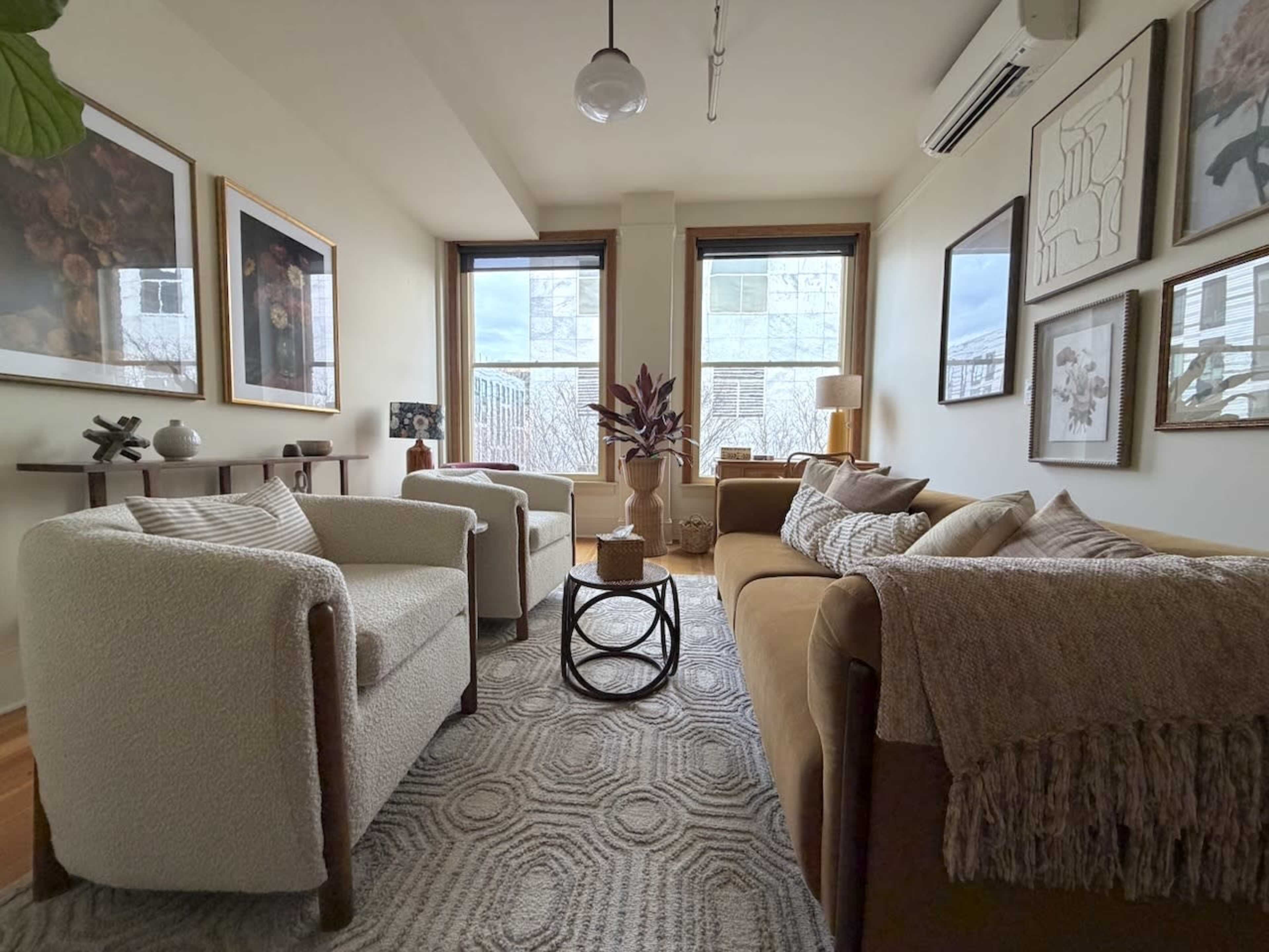 A cozy living room features two armchairs, a sofa, and various framed artworks on the walls.