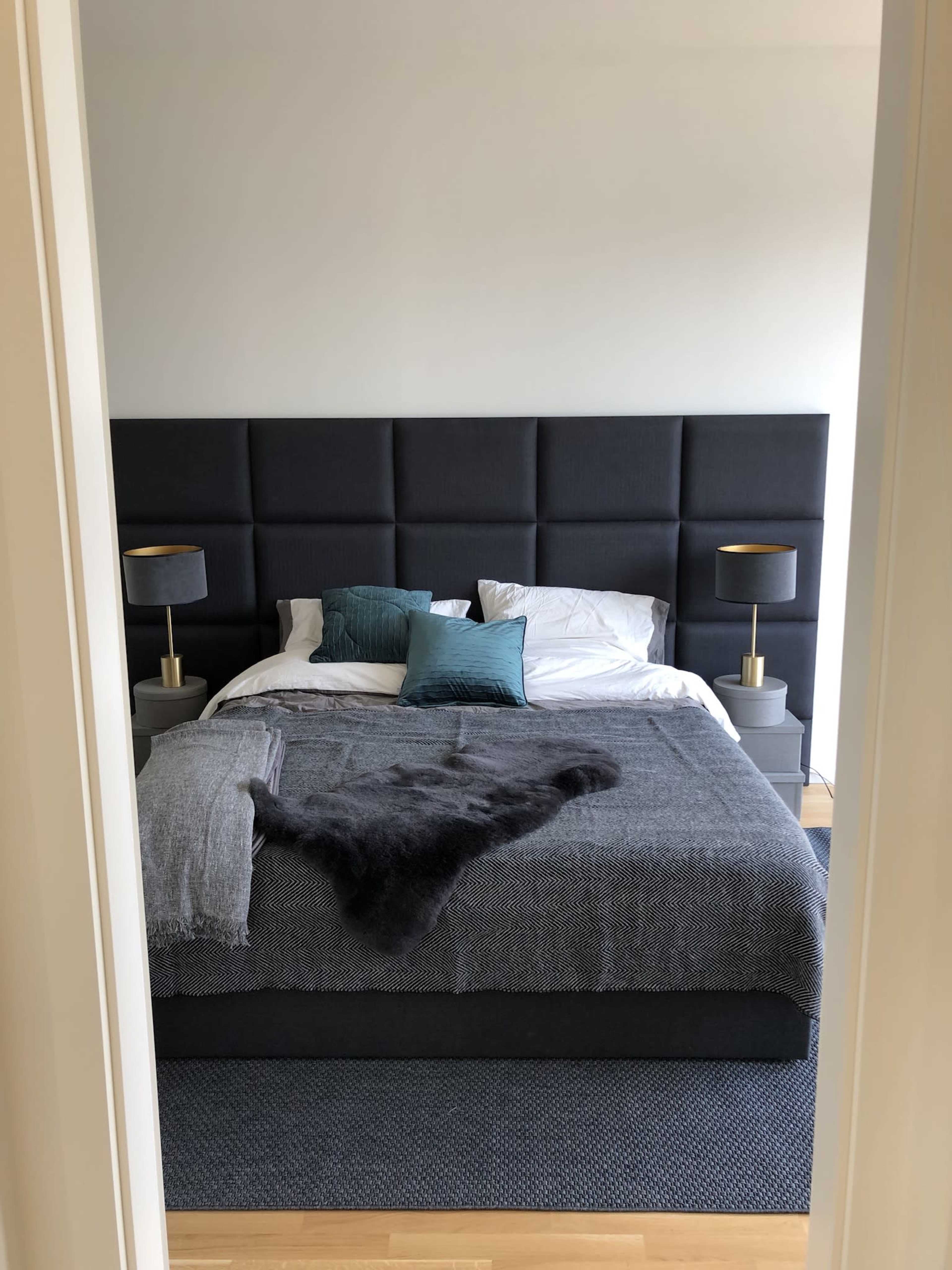 A neatly made bed with dark headboard and decorative pillows is viewed through an open doorway.