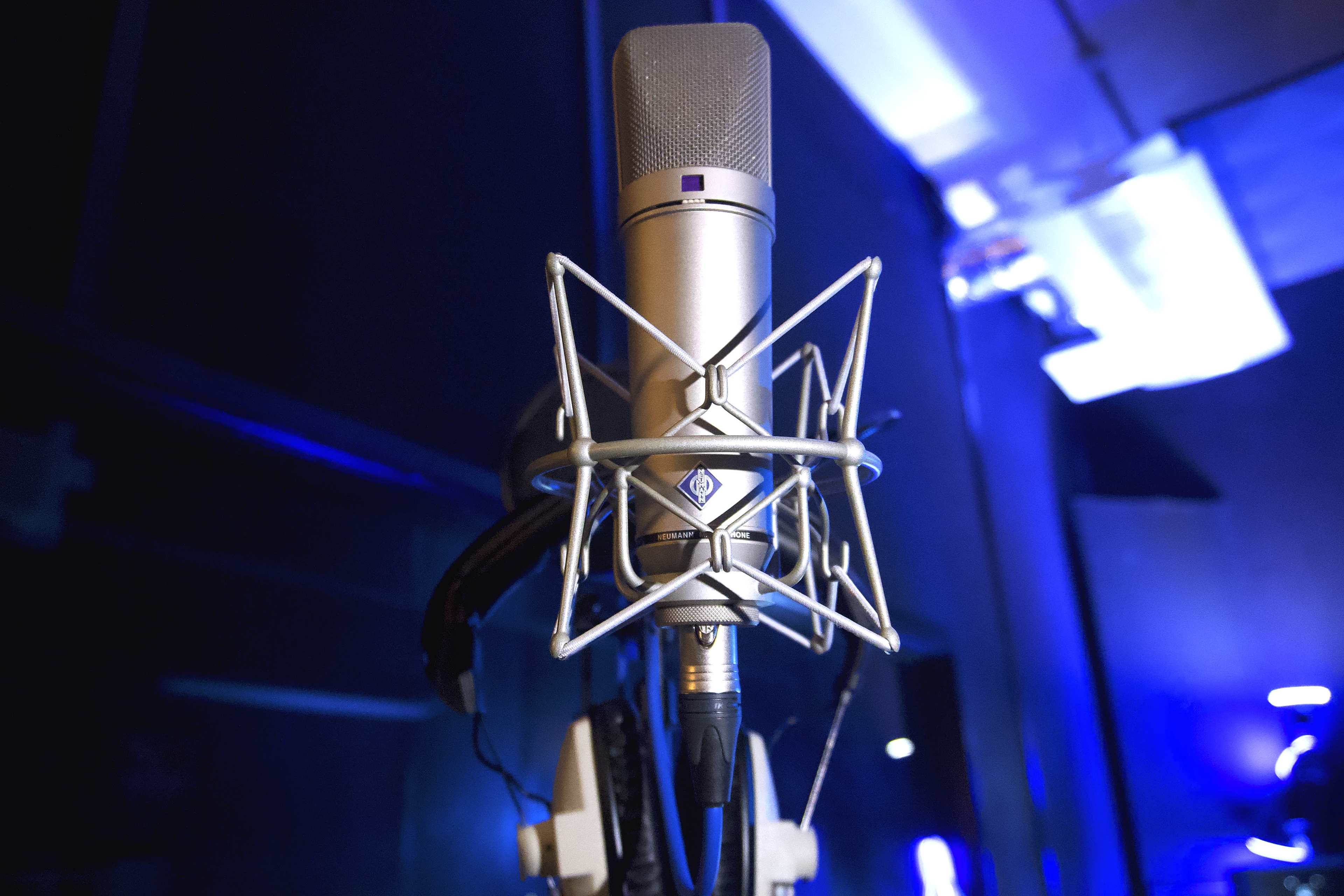 A silver microphone is mounted on a stand, surrounded by a dark studio environment with soft blue lighting.