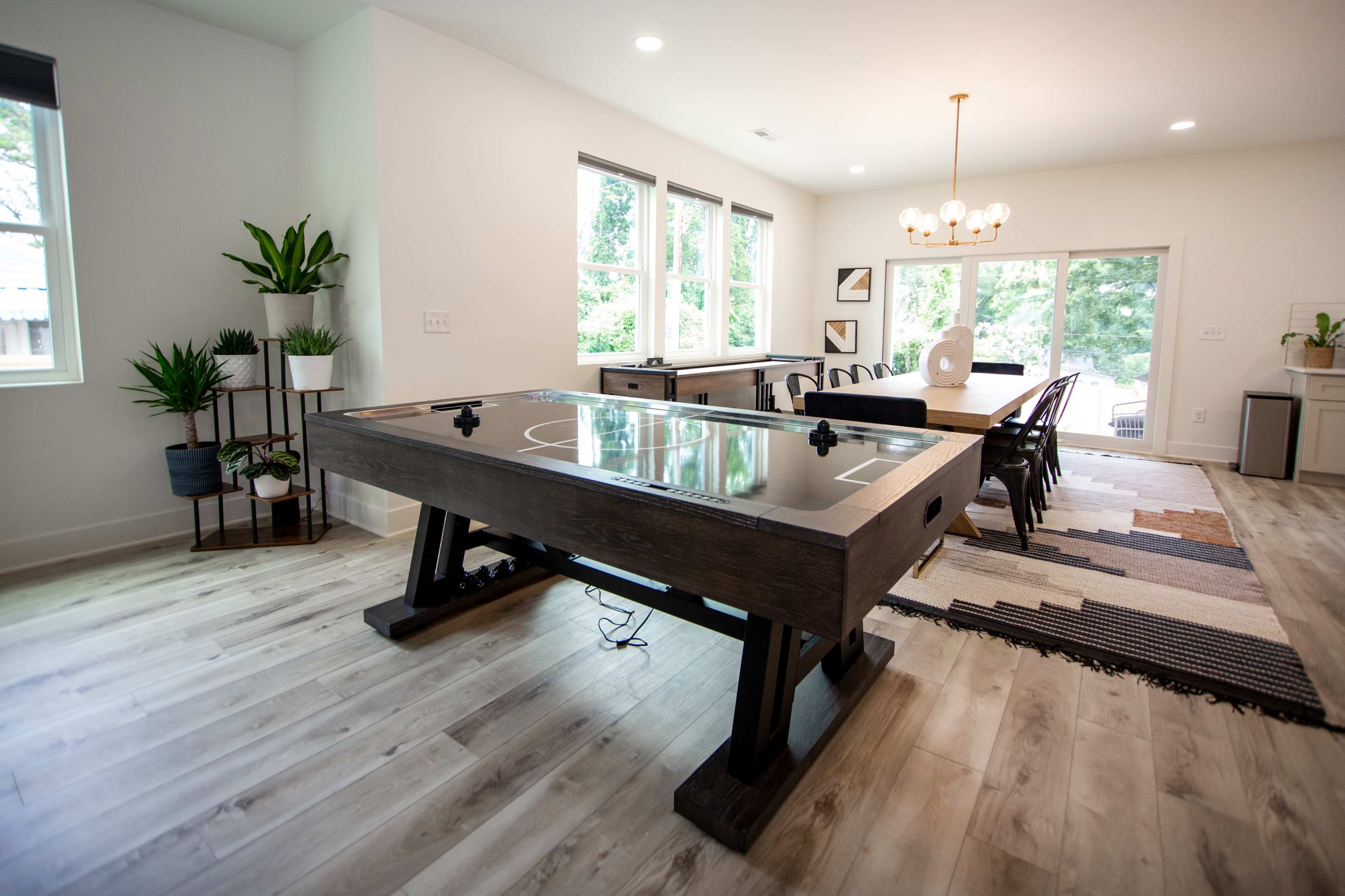 A modern dining area features a large air hockey table, a dining table with chairs, and windows that allow natural light to fill the space.