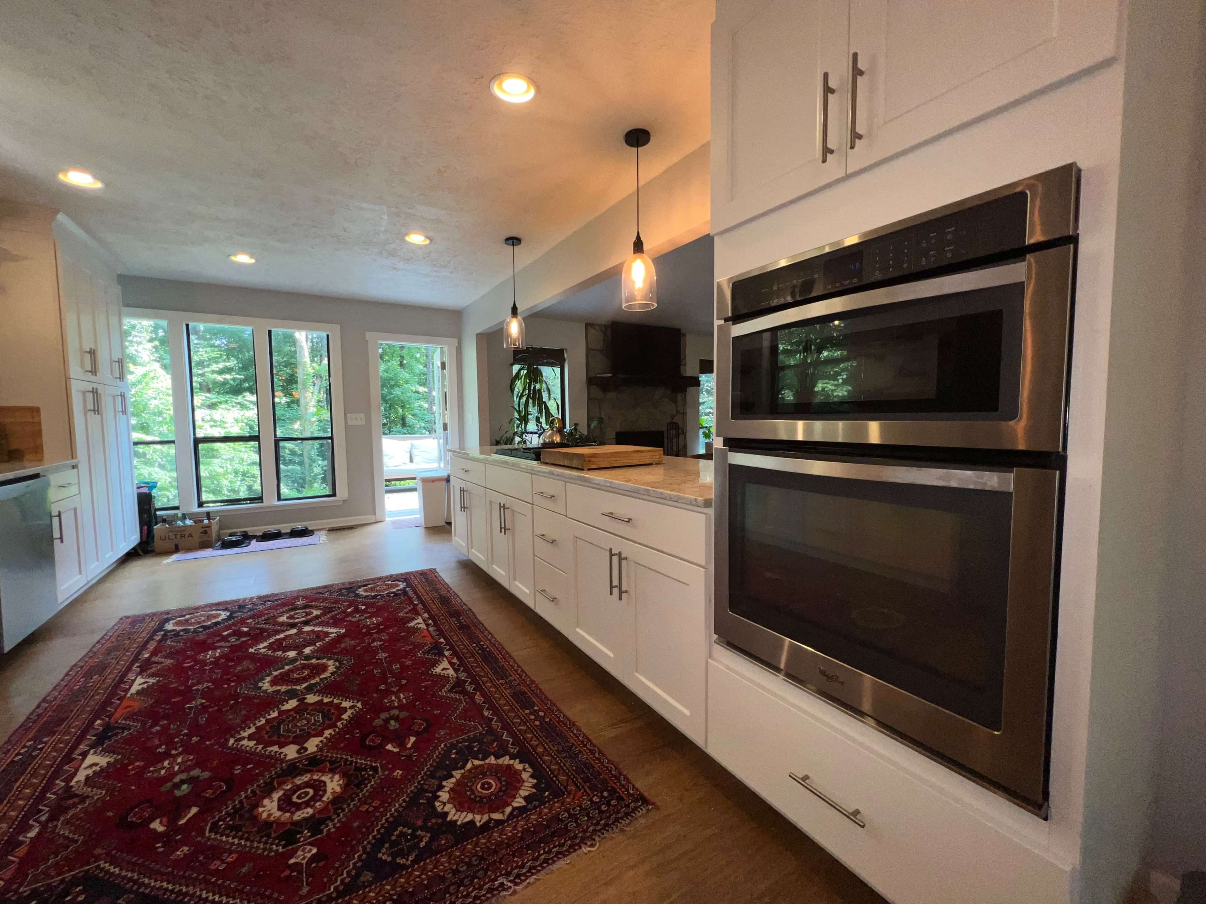 A modern kitchen with white cabinets, stainless steel appliances, and a decorative rug on the wooden floor.