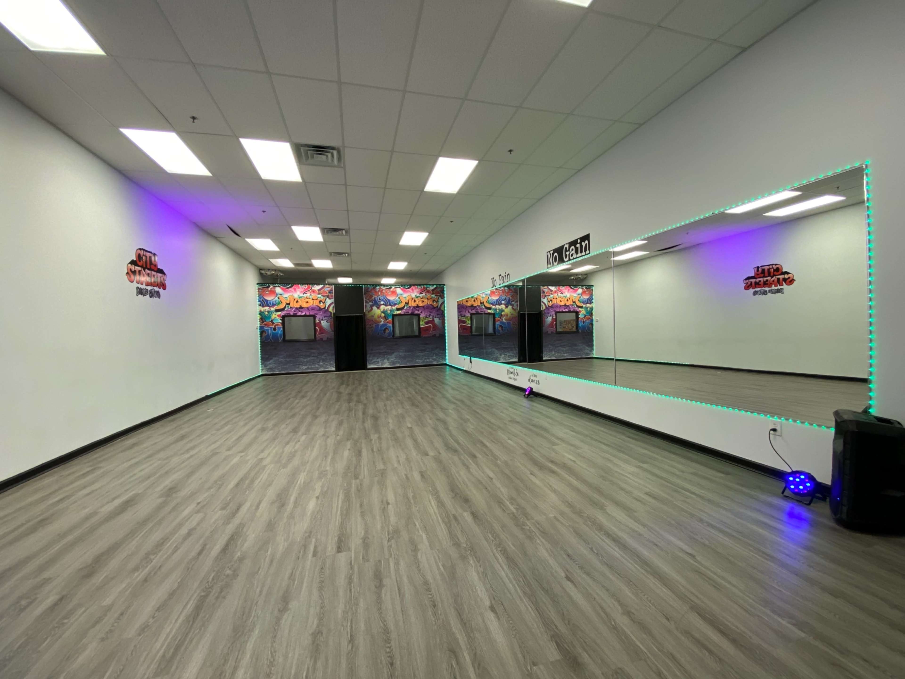 A spacious dance studio with mirrored walls and colorful mural artwork in the background.