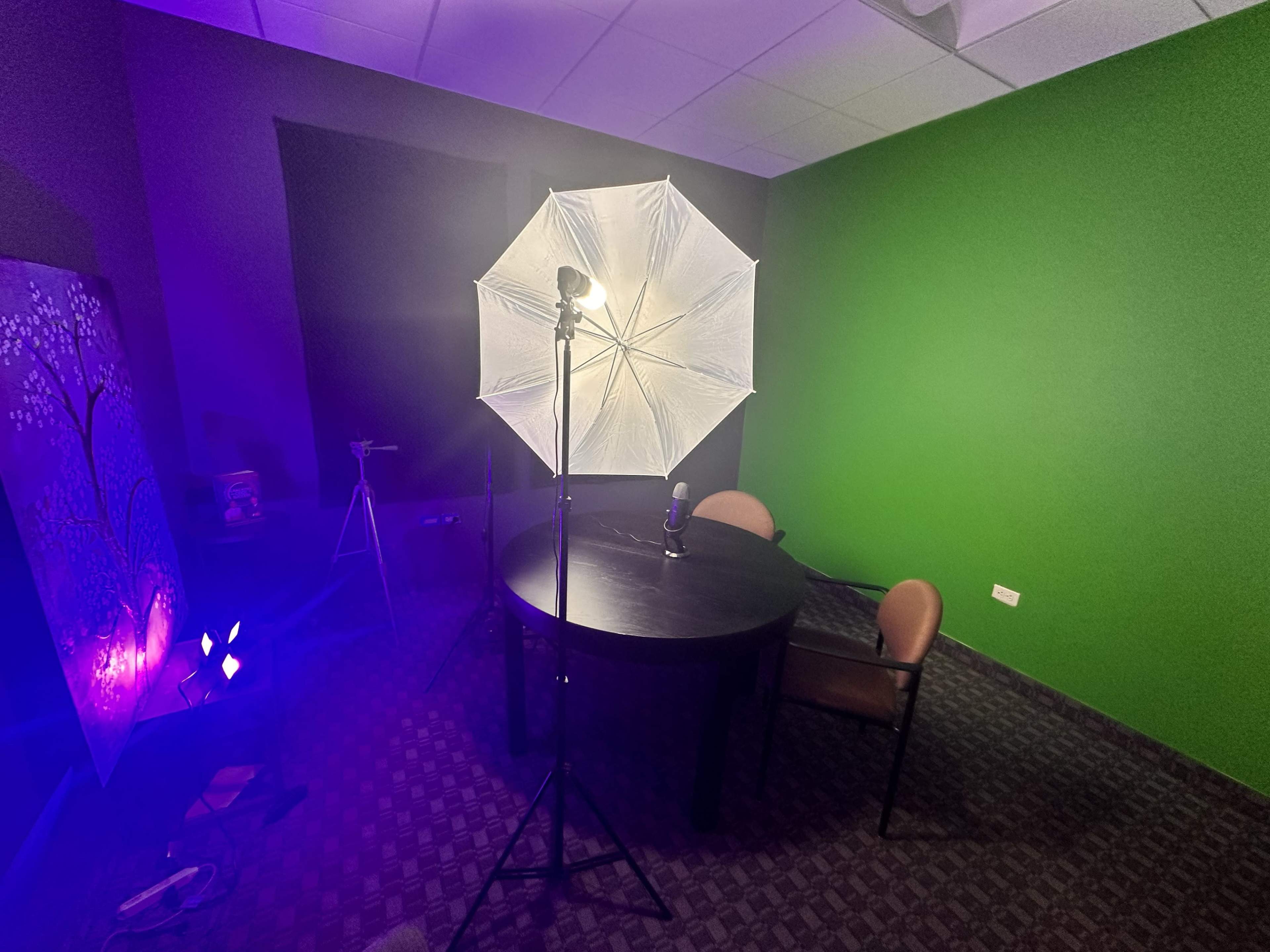 A microphone sits on a table illuminated by an umbrella light in a room featuring a green wall.
