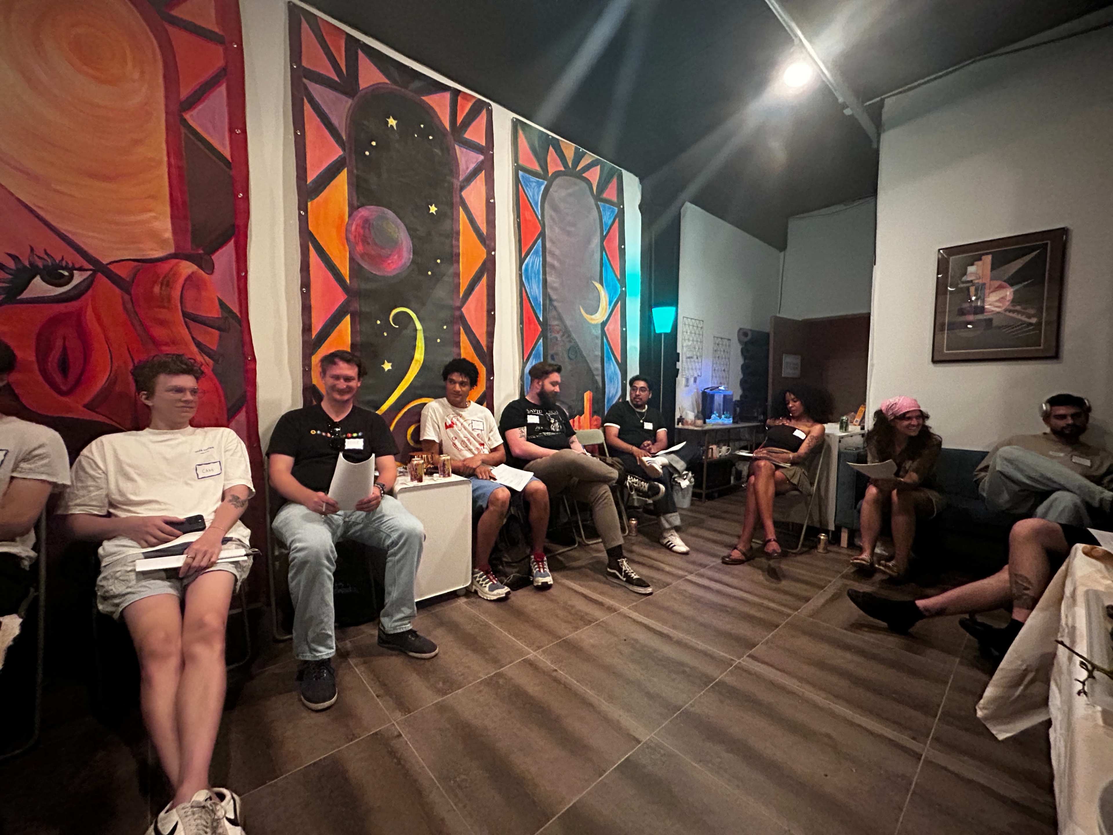 A group of people sits in a bright room adorned with colorful artwork and engaging in conversation.