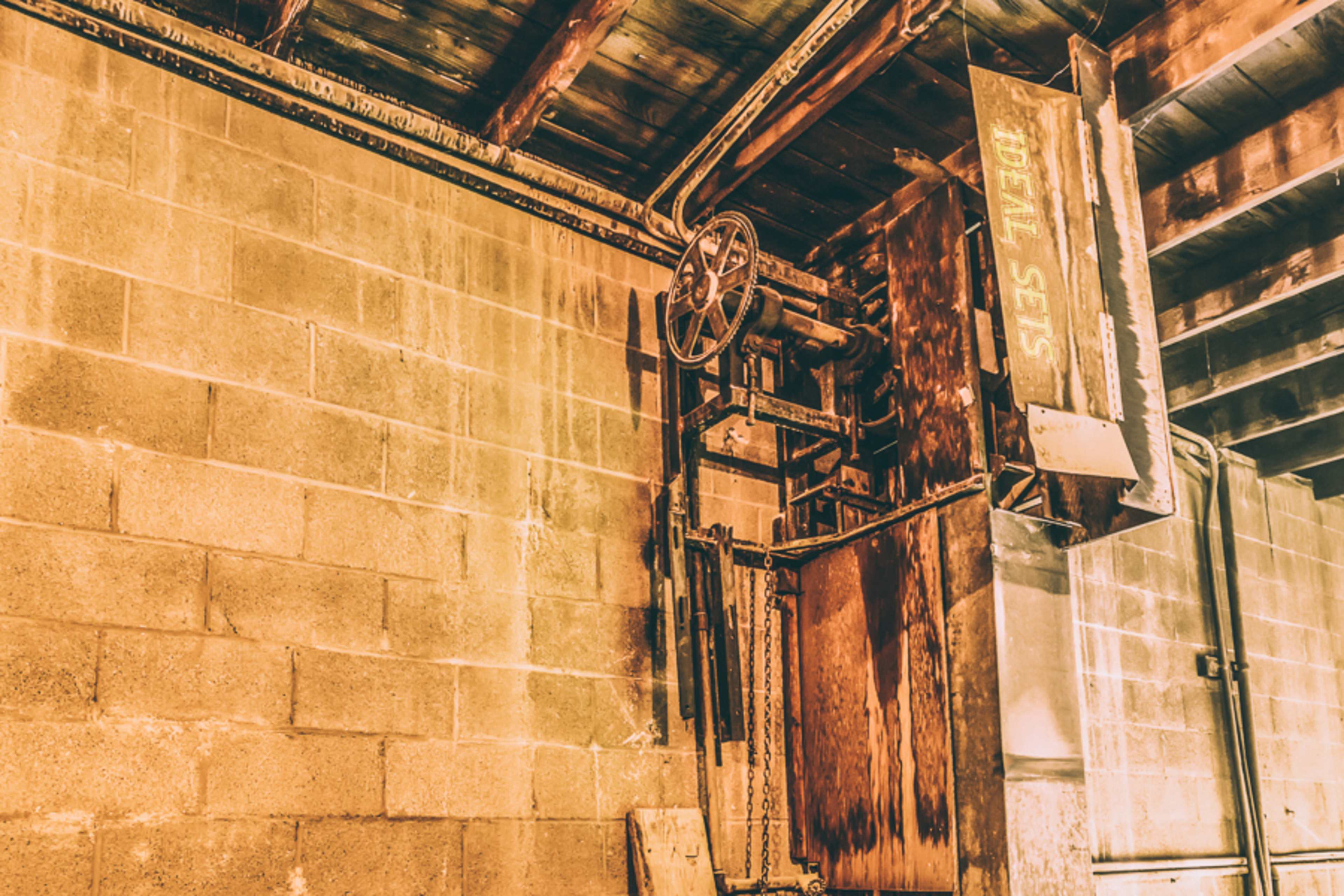 An old metal elevator apparatus mounted on a concrete wall in a dimly lit industrial space.