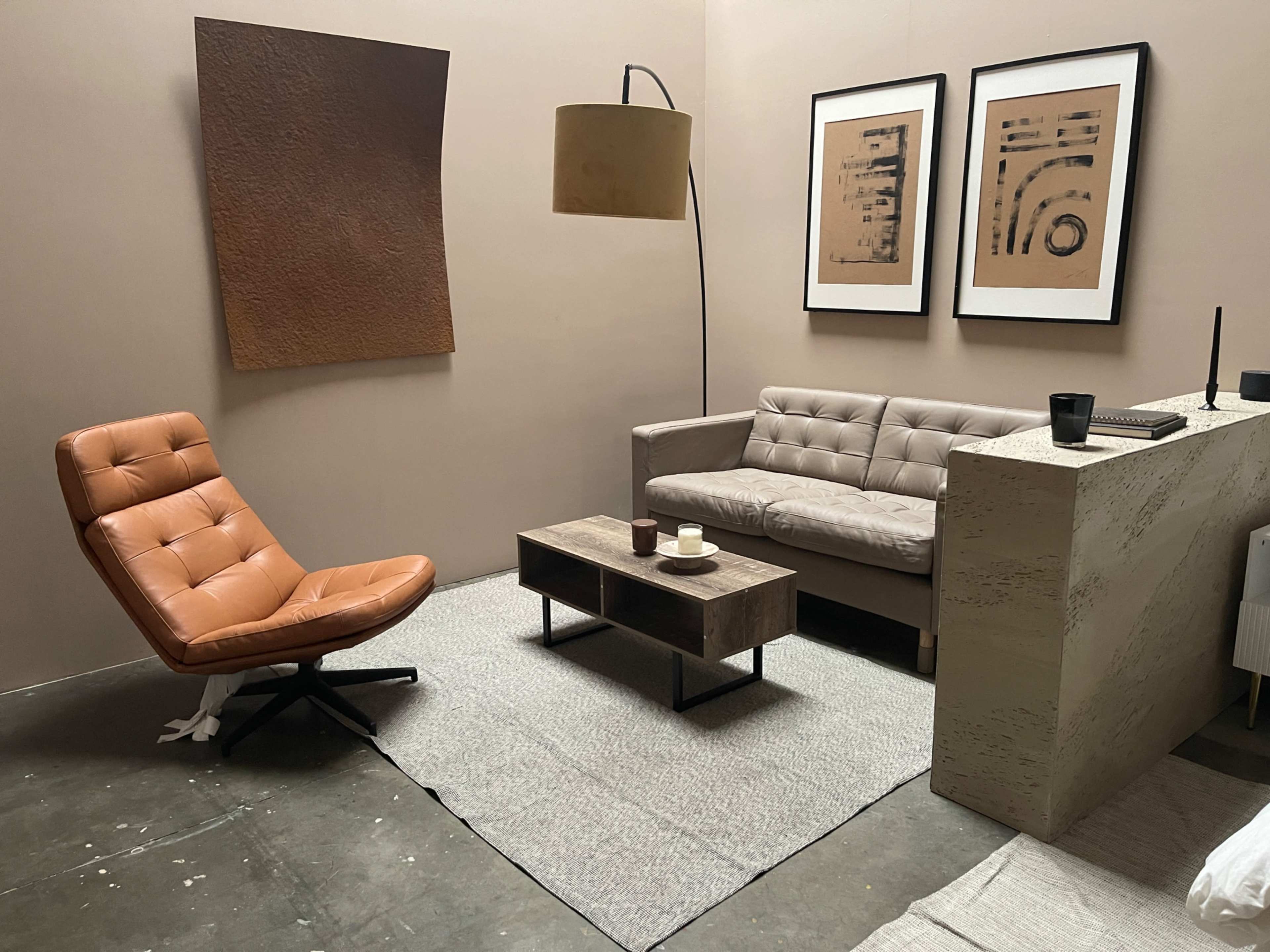 A modern living room setup featuring a brown leather chair, a gray sofa, a wooden coffee table, and framed artwork on the wall.