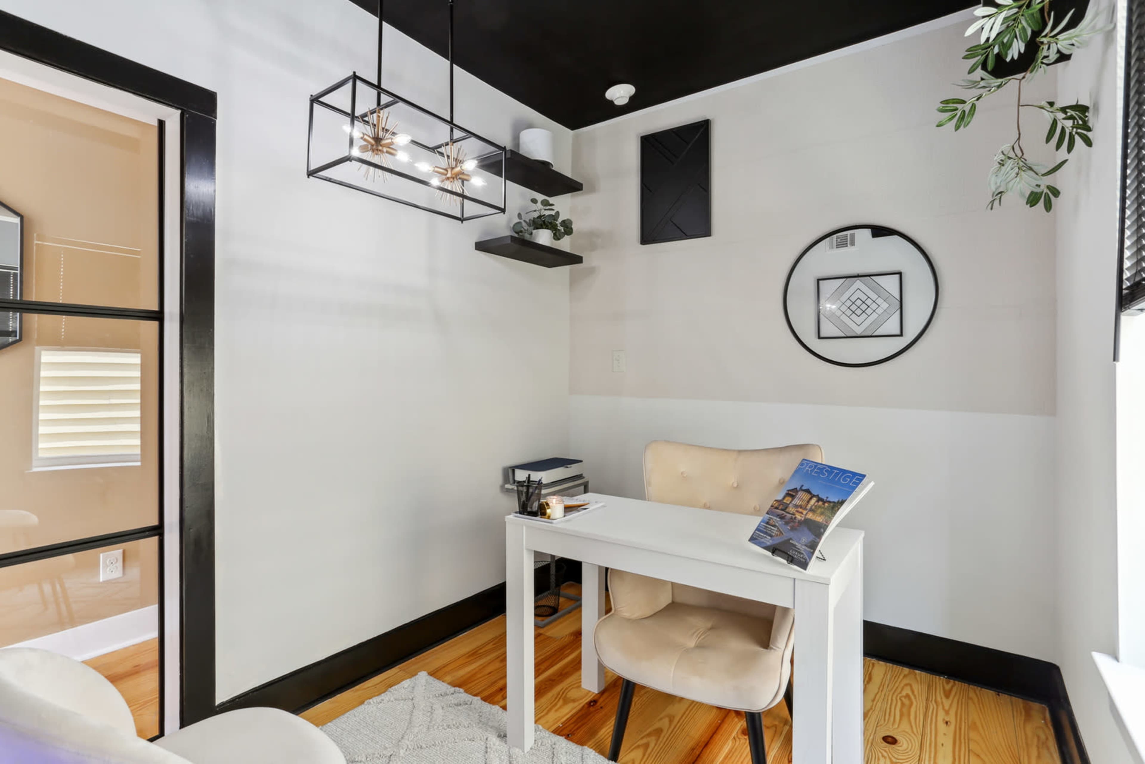 A modern home office with a small white desk, a chair, and decorative elements like a hanging light fixture and plants.