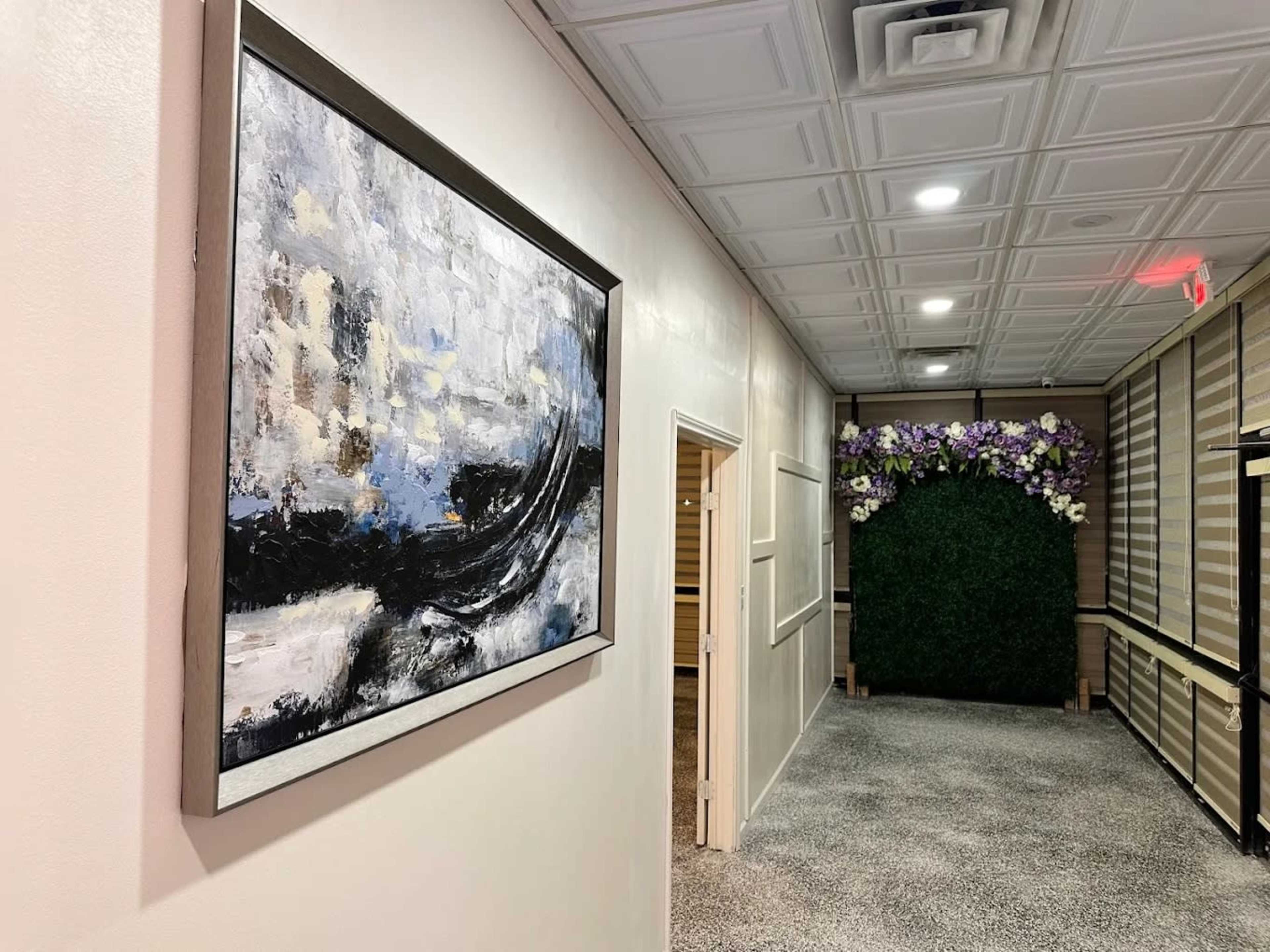 A hallway features a framed abstract painting on the left wall, leading to a door and a greenery display at the far end.