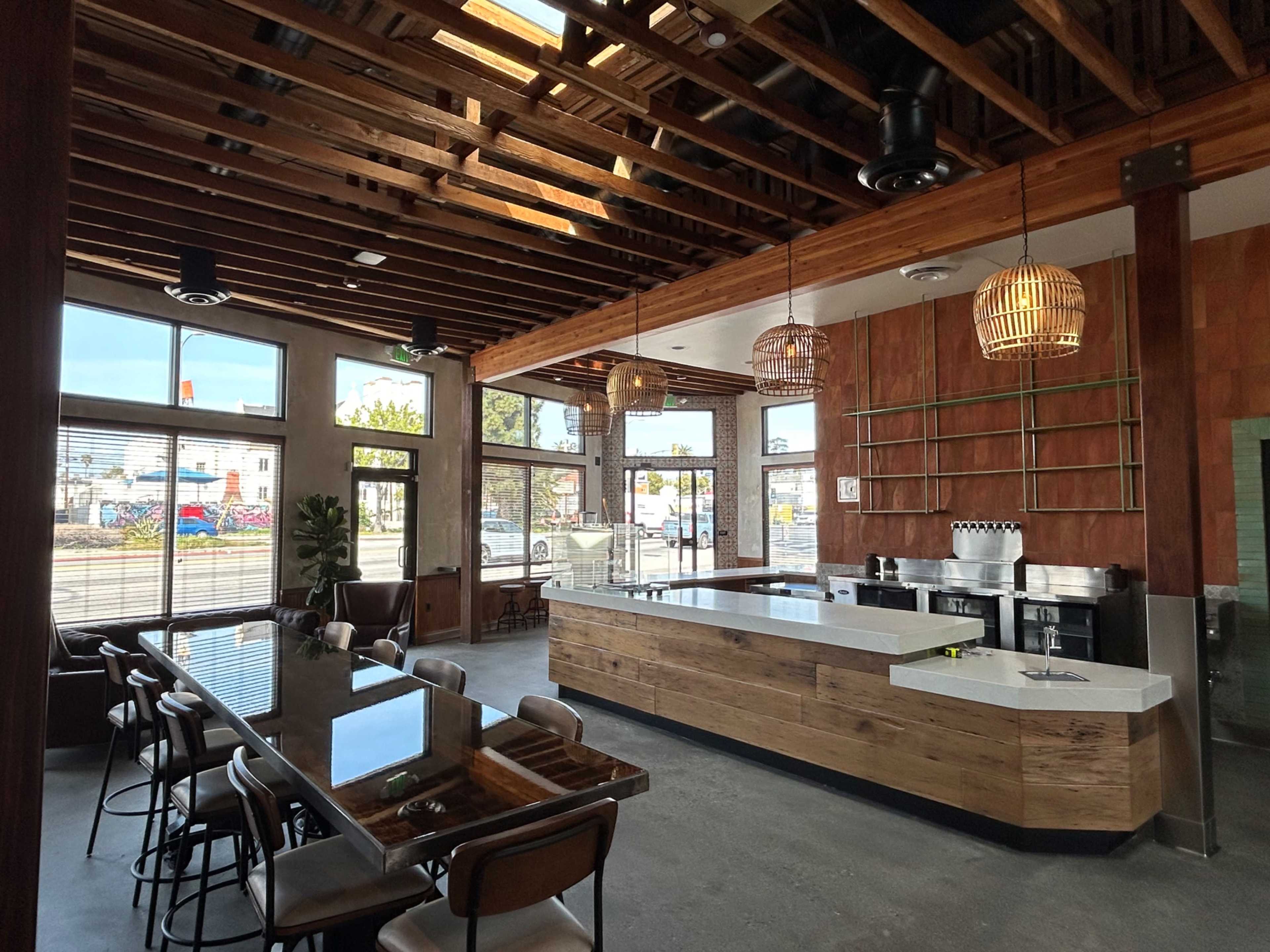 A modern café interior featuring a wooden counter, a long communal table, and large windows allowing natural light to enter the space.