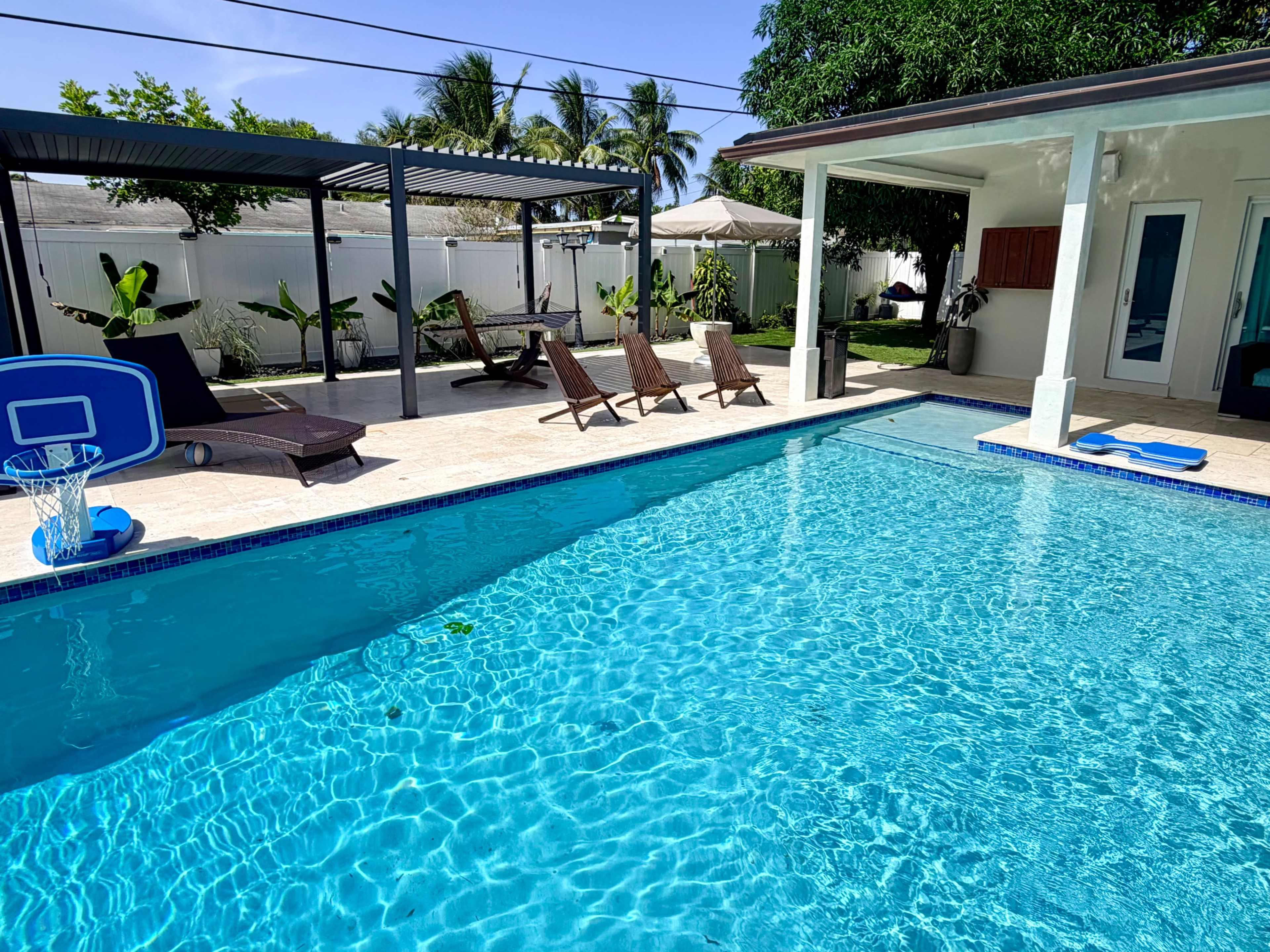 A swimming pool with clear blue water is surrounded by lounge chairs and tropical landscaping.