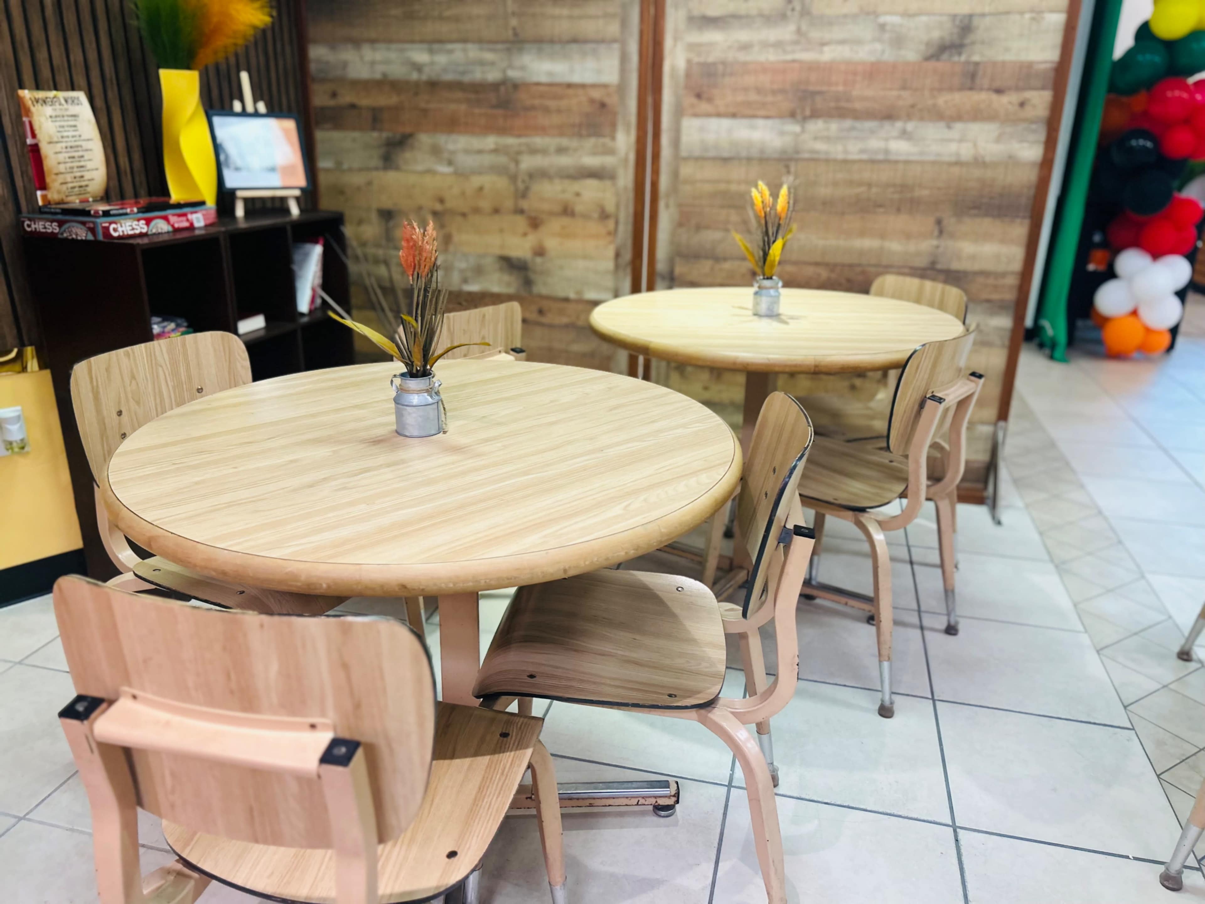 Two wooden tables with small vases of flowers are placed in a cafe setting featuring wooden wall panels.