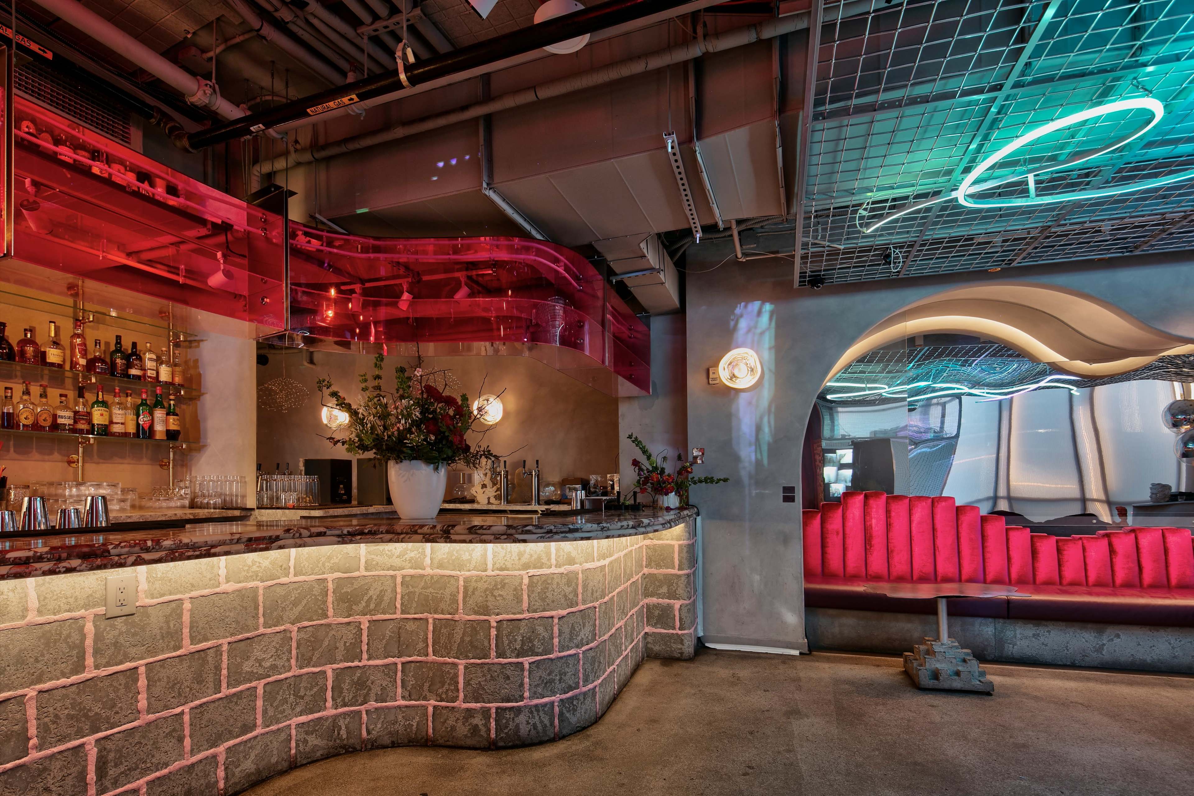 The image features a modern bar area with a curved countertop, colorful LED lighting, and a seating area designed with futuristic elements.