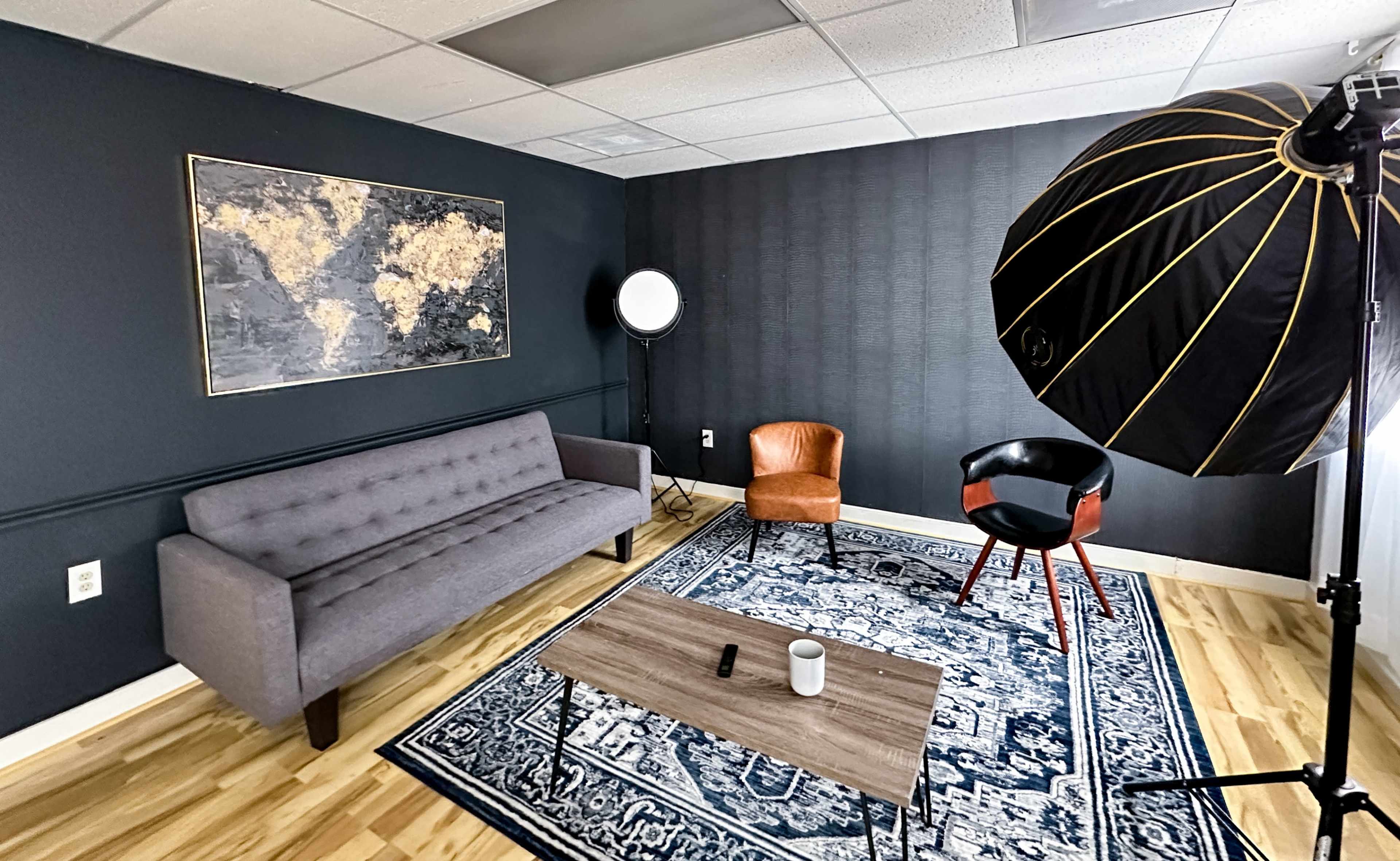 A modern interior with a gray sofa, an orange chair, a black chair, a coffee table, and a large world map on the wall, illuminated by studio lighting.