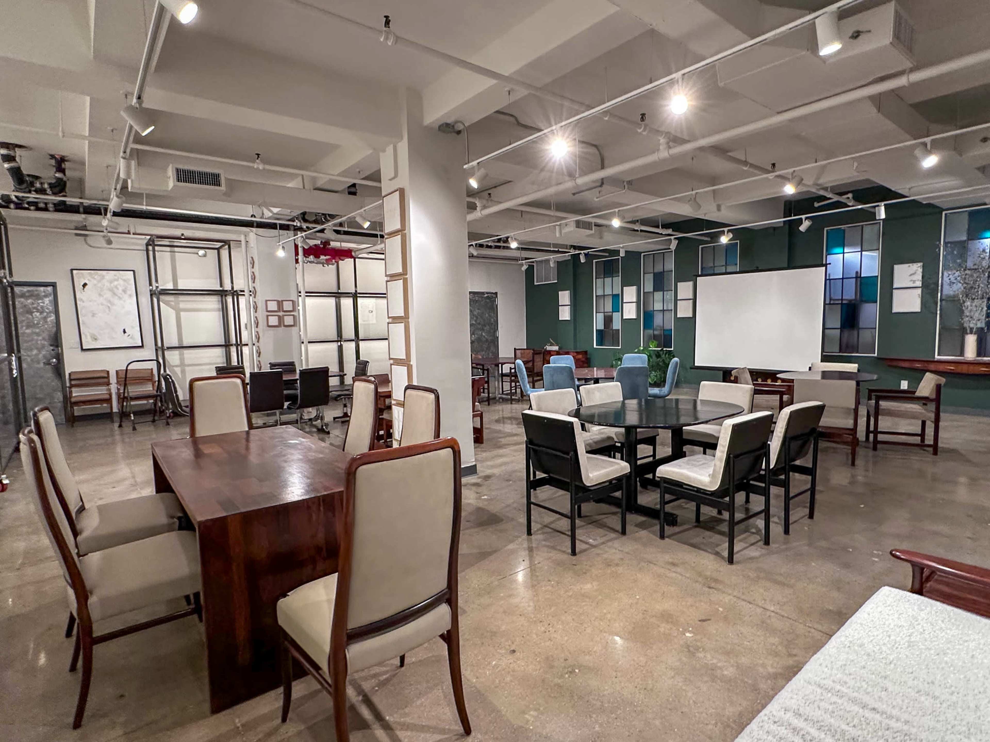 The image shows a spacious, modern office or meeting area with multiple tables and chairs arranged throughout the room.