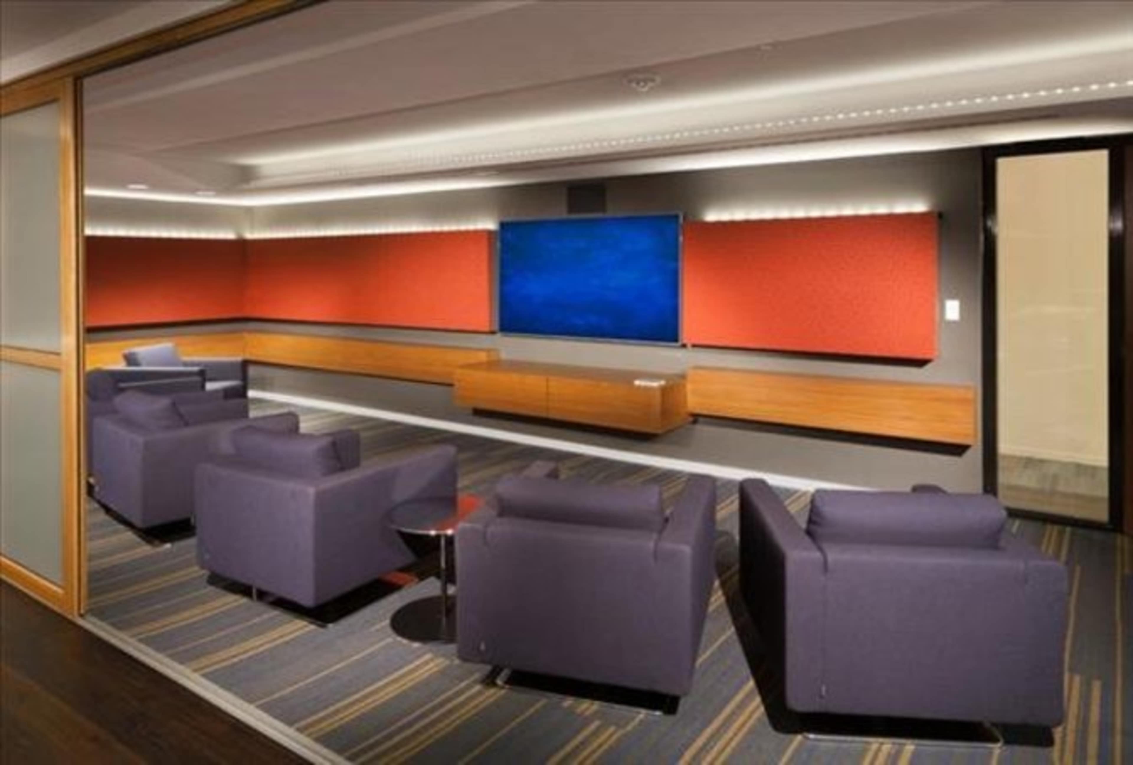 A modern lounge area with purple seating opposite a large television mounted on a wall between red acoustic panels.