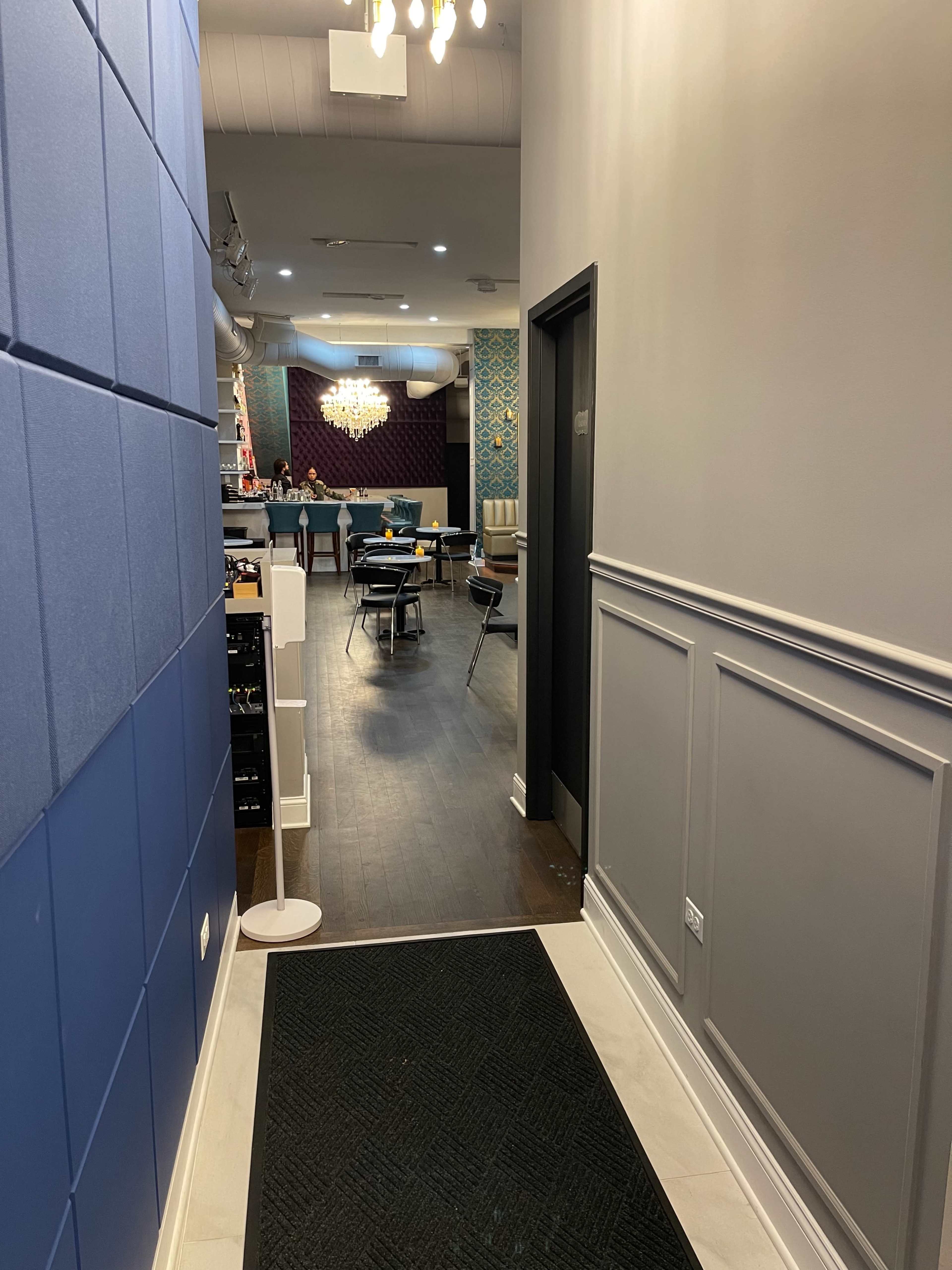 A hallway leads to a dining area with tables and chairs, featuring decorative walls and a chandelier.