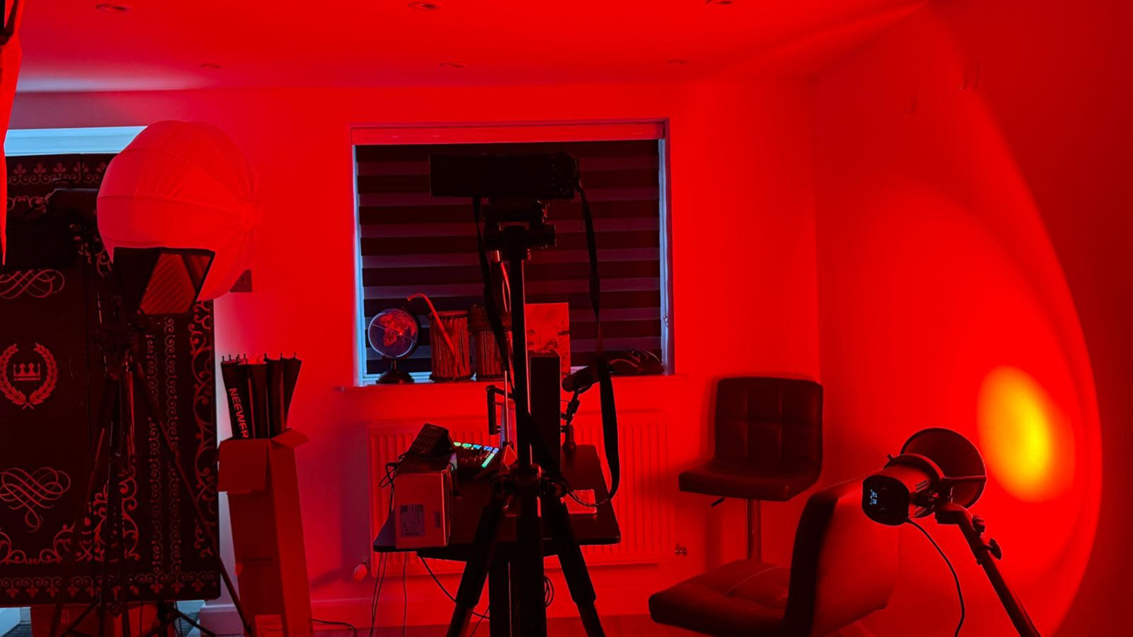 The image shows a room illuminated with red light, featuring various photography equipment and a chair.