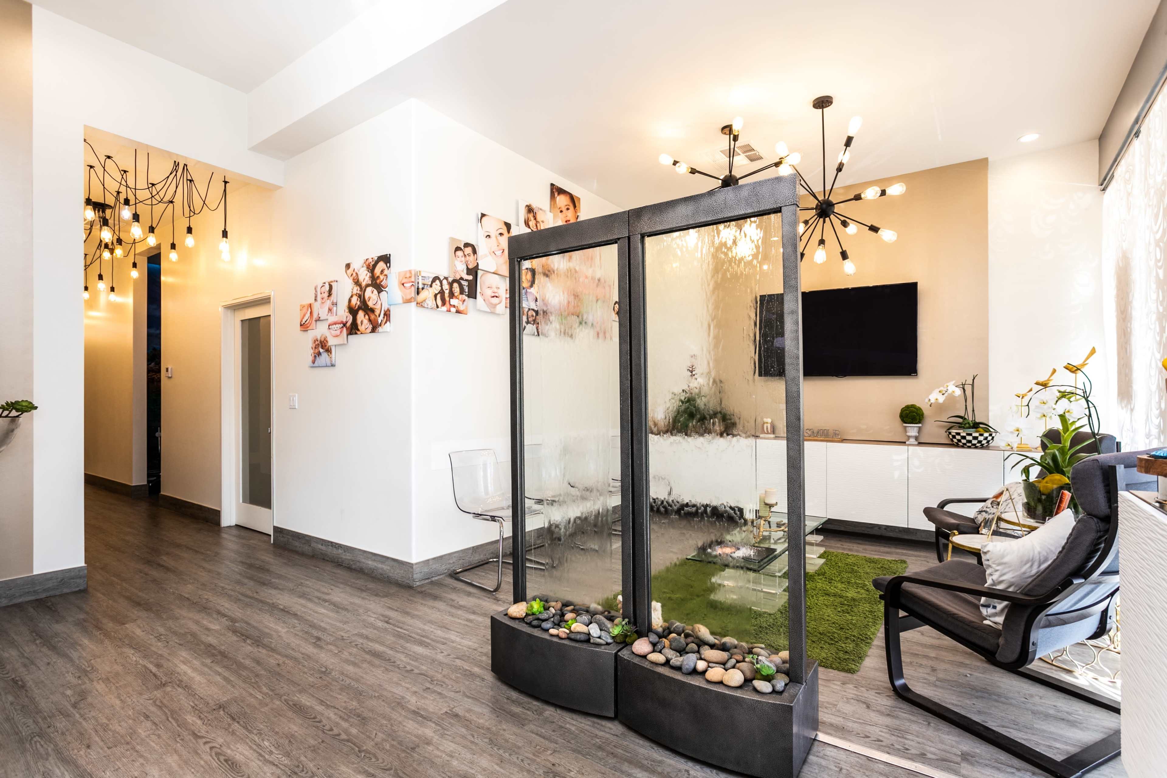 A modern waiting area with sleek furniture, a water feature, and various family photos displayed on the walls.