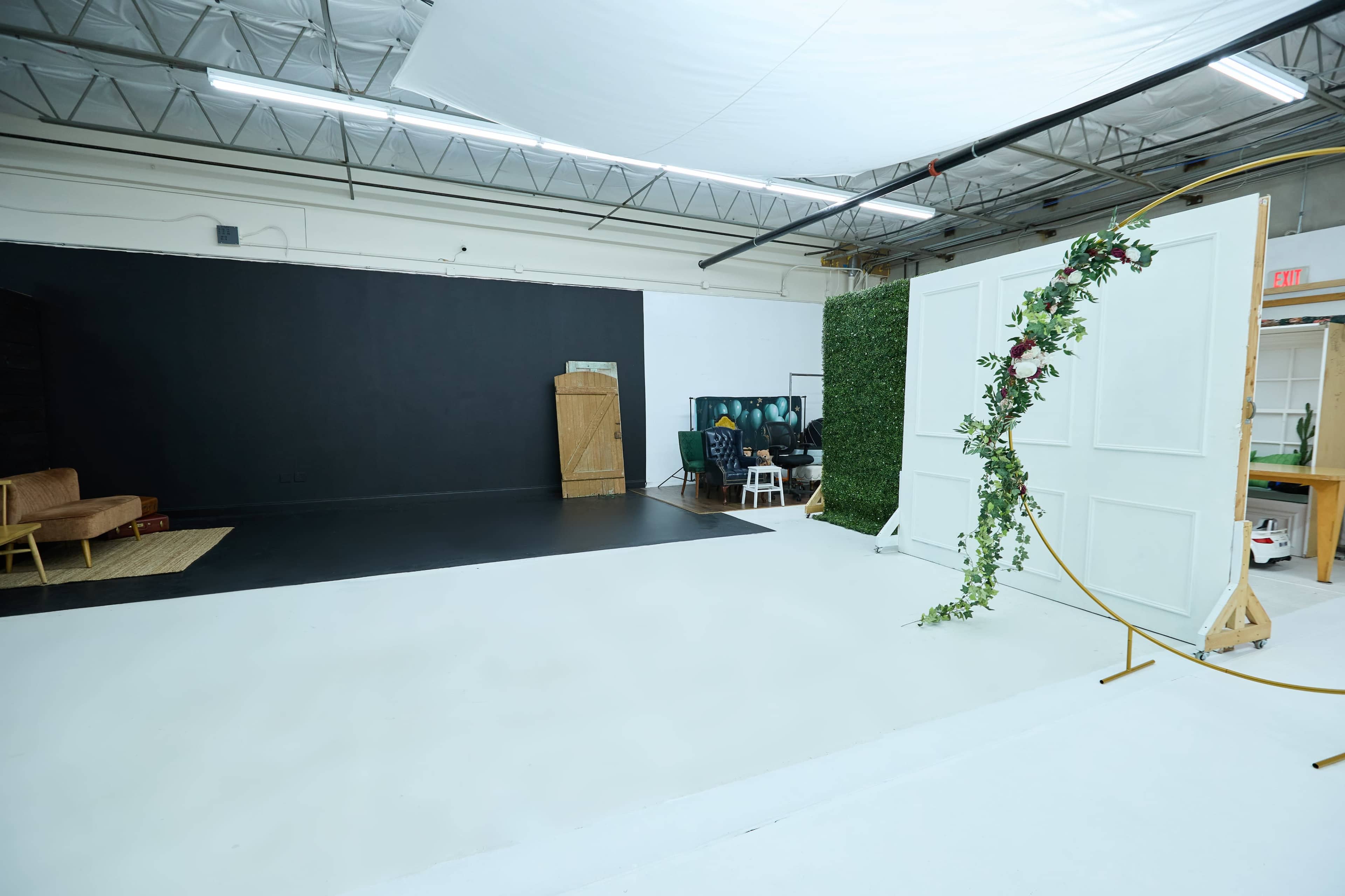 A spacious studio with a simple white floor, a black backdrop on one side, and a set of white doors decorated with greenery.