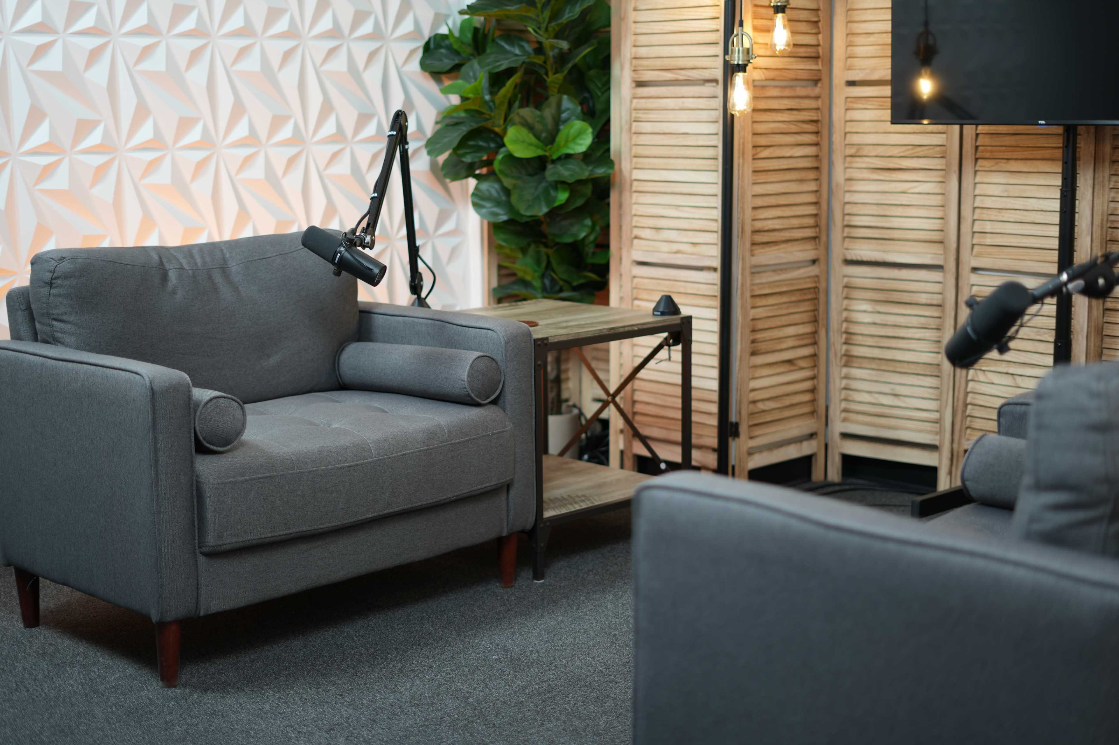 The image features a cozy seating area with two gray armchairs, a wooden side table, and a backdrop of a decorative partition and green plants.