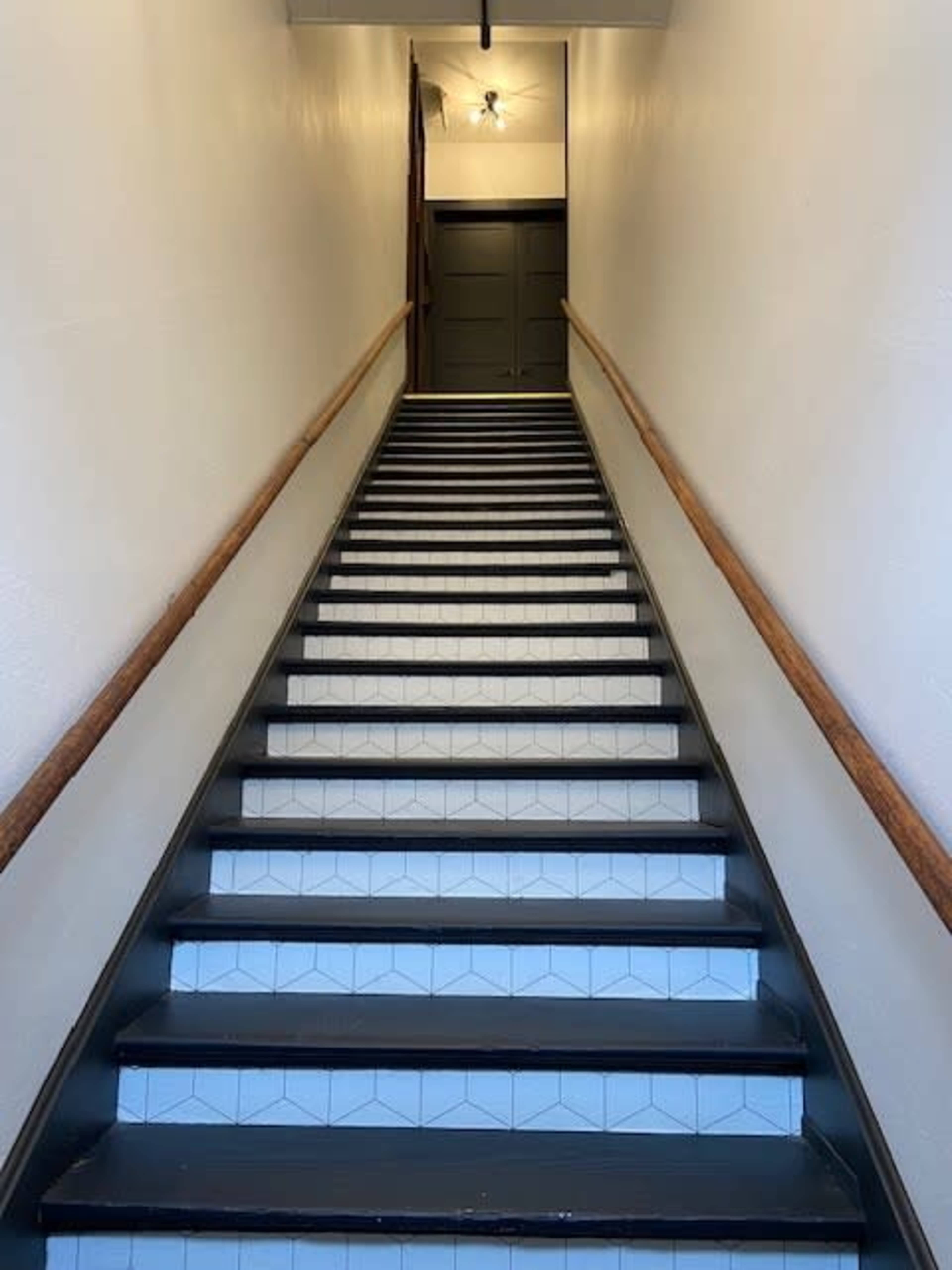 A staircase with wooden handrails leads up to a door at the top in a well-lit corridor.