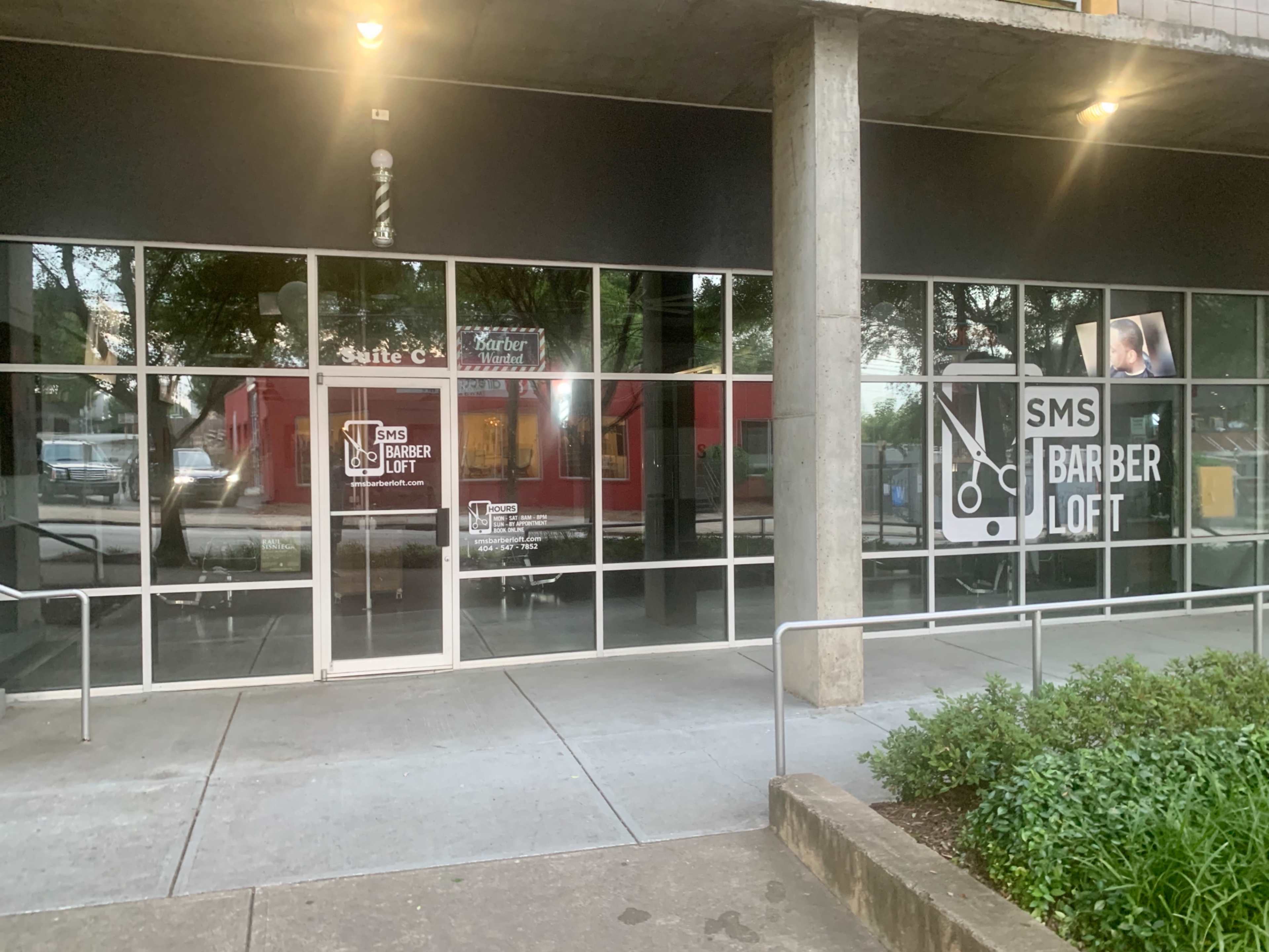 The image shows the exterior of a barbershop named "SMS Barber Loft," featuring large glass windows and a concrete entrance.