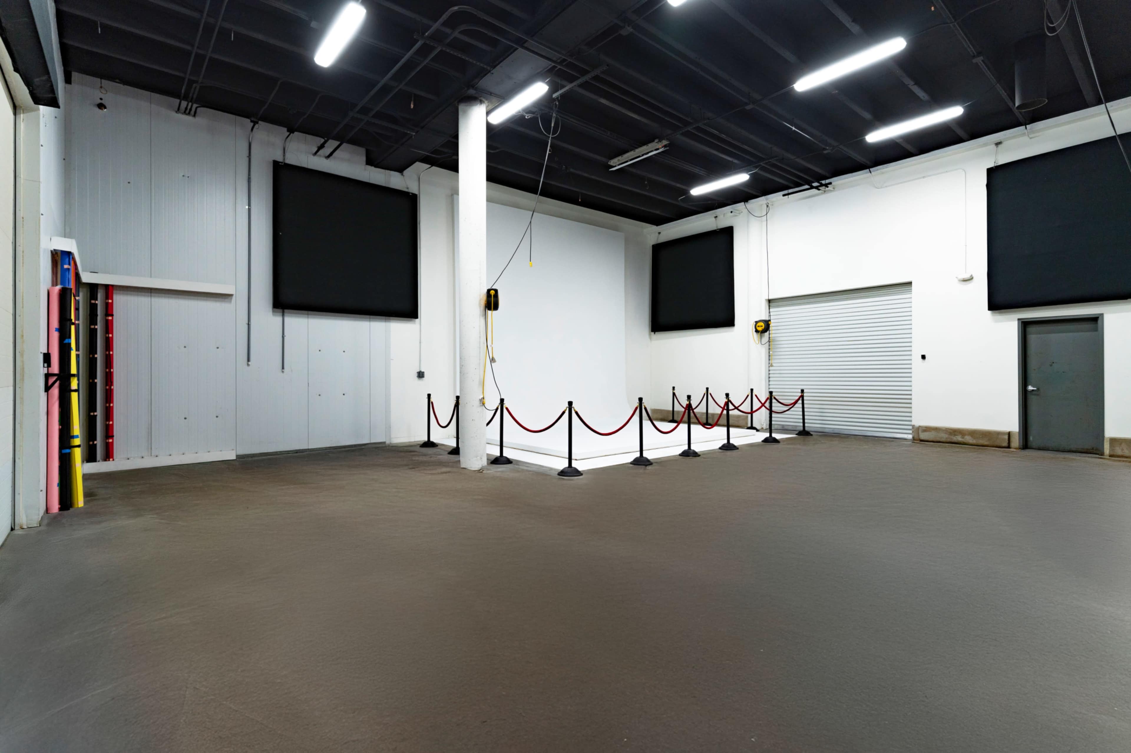 The image shows a large, empty indoor space with a smooth floor, white walls, and two large screens mounted on the walls.