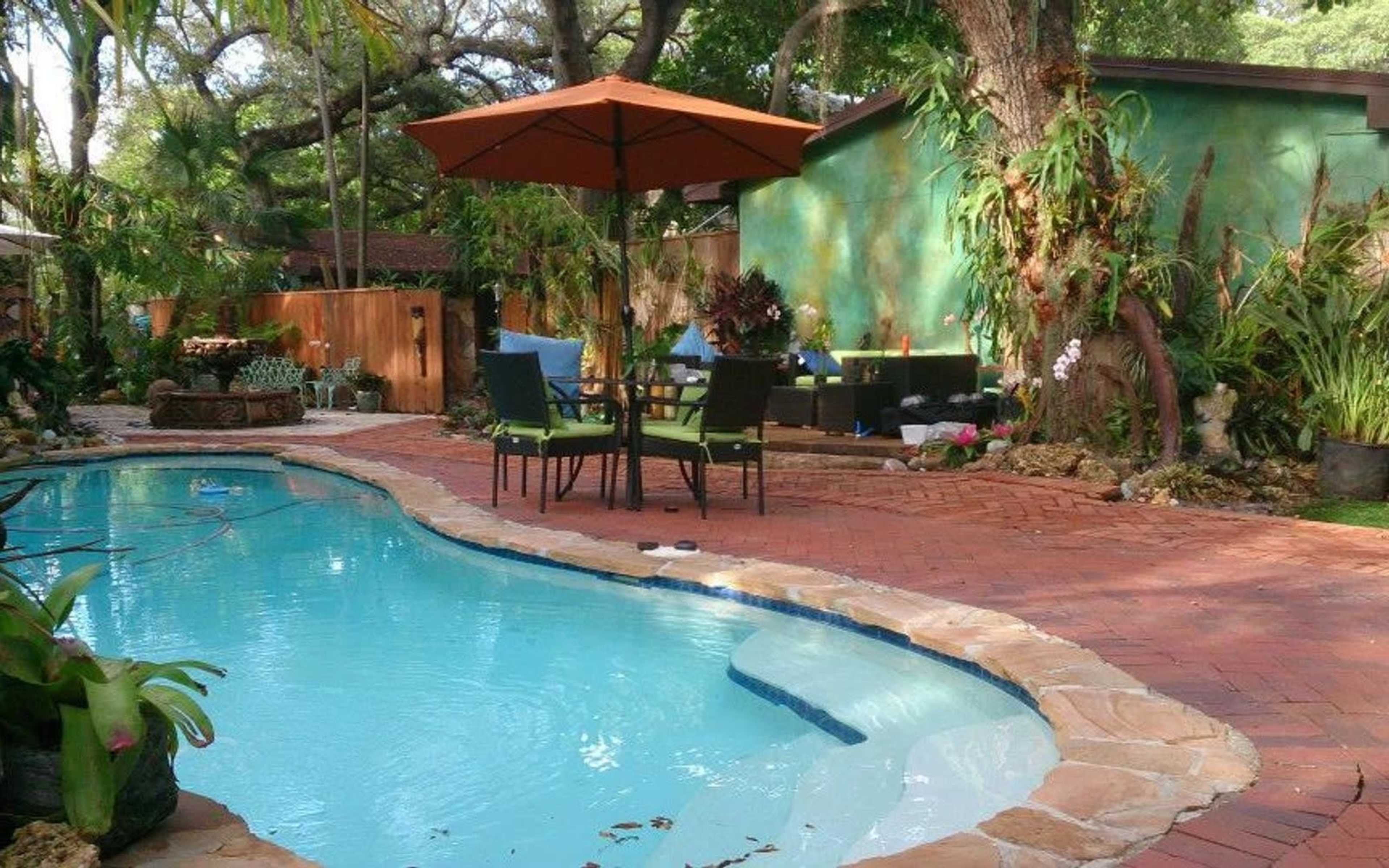 A swimming pool with a curved edge is surrounded by a patio featuring outdoor furniture and tropical plants.