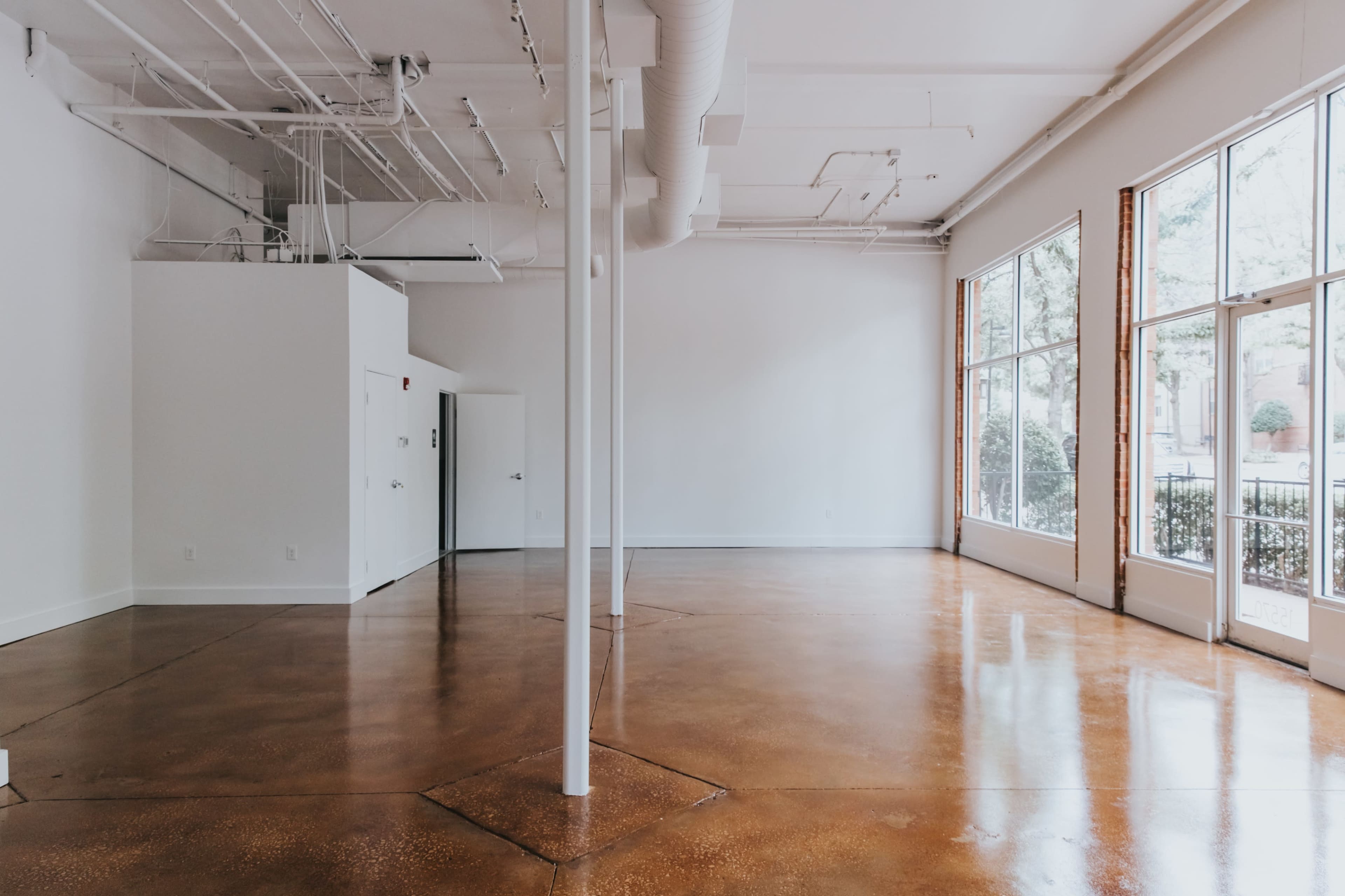 The image shows a spacious, empty room with polished concrete floors and large windows allowing natural light to fill the space.