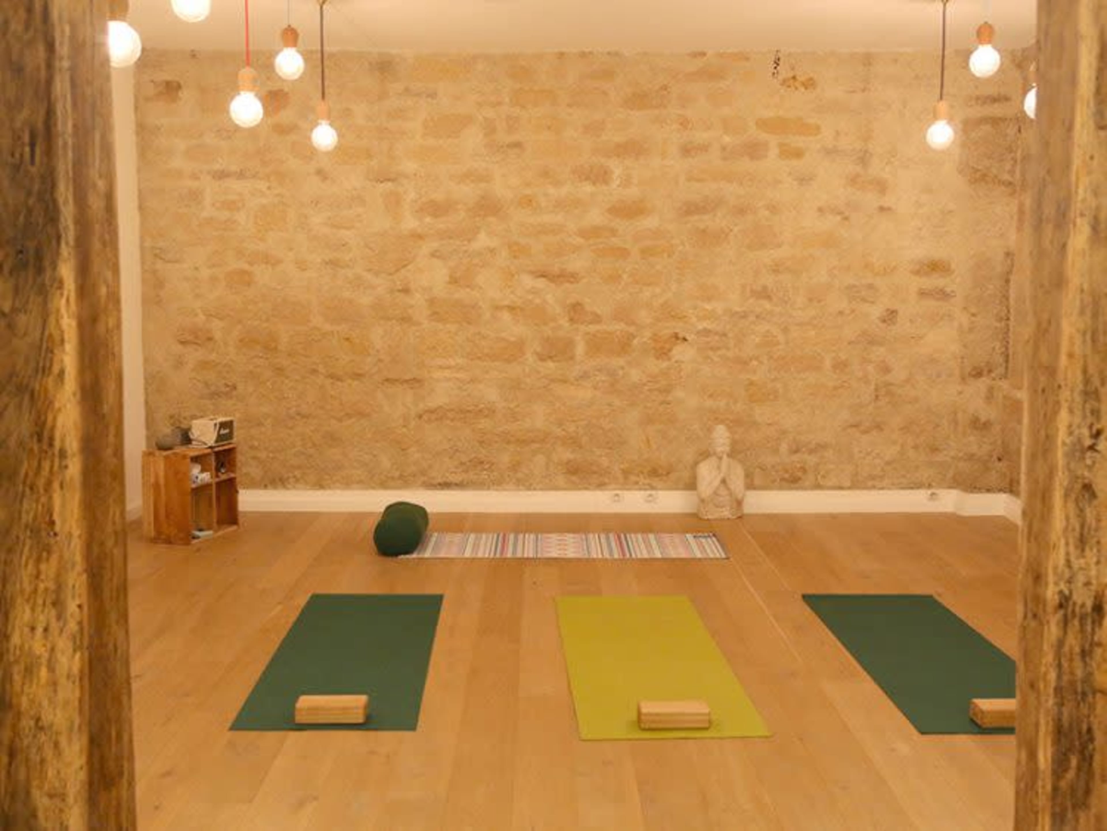 A yoga studio with three yoga mats and minimal decor, including a statue and shelves against a stone wall.