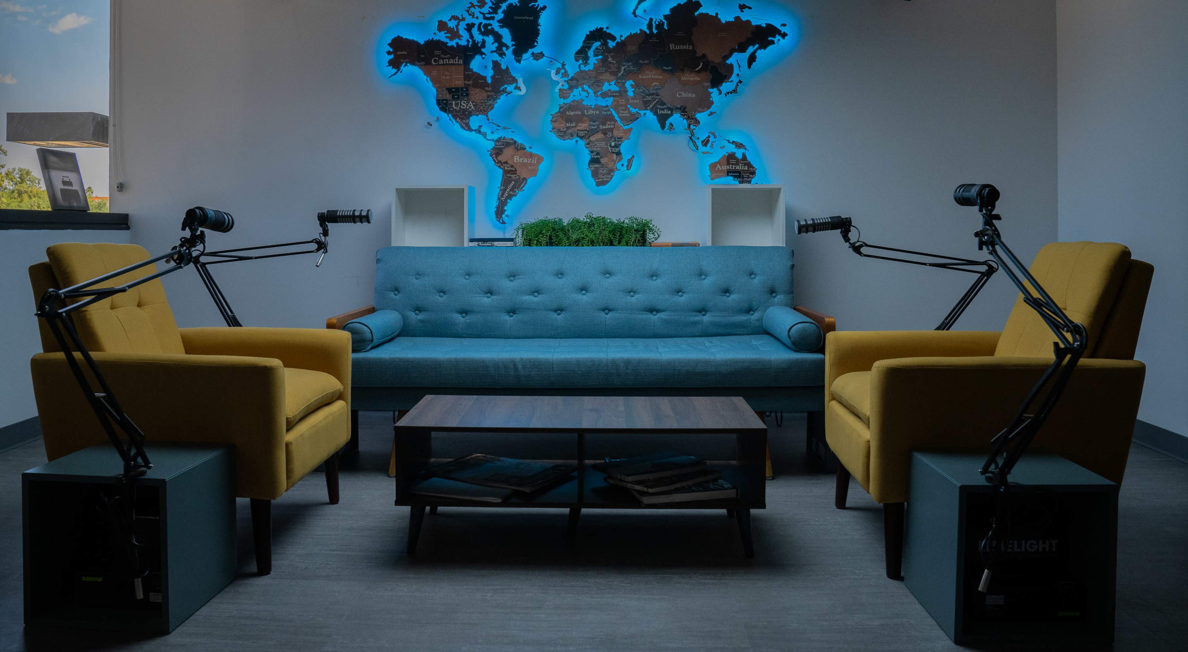 The image shows a modern seating area with a blue sofa, two yellow armchairs, a wooden coffee table, and a world map illuminated behind the furniture.