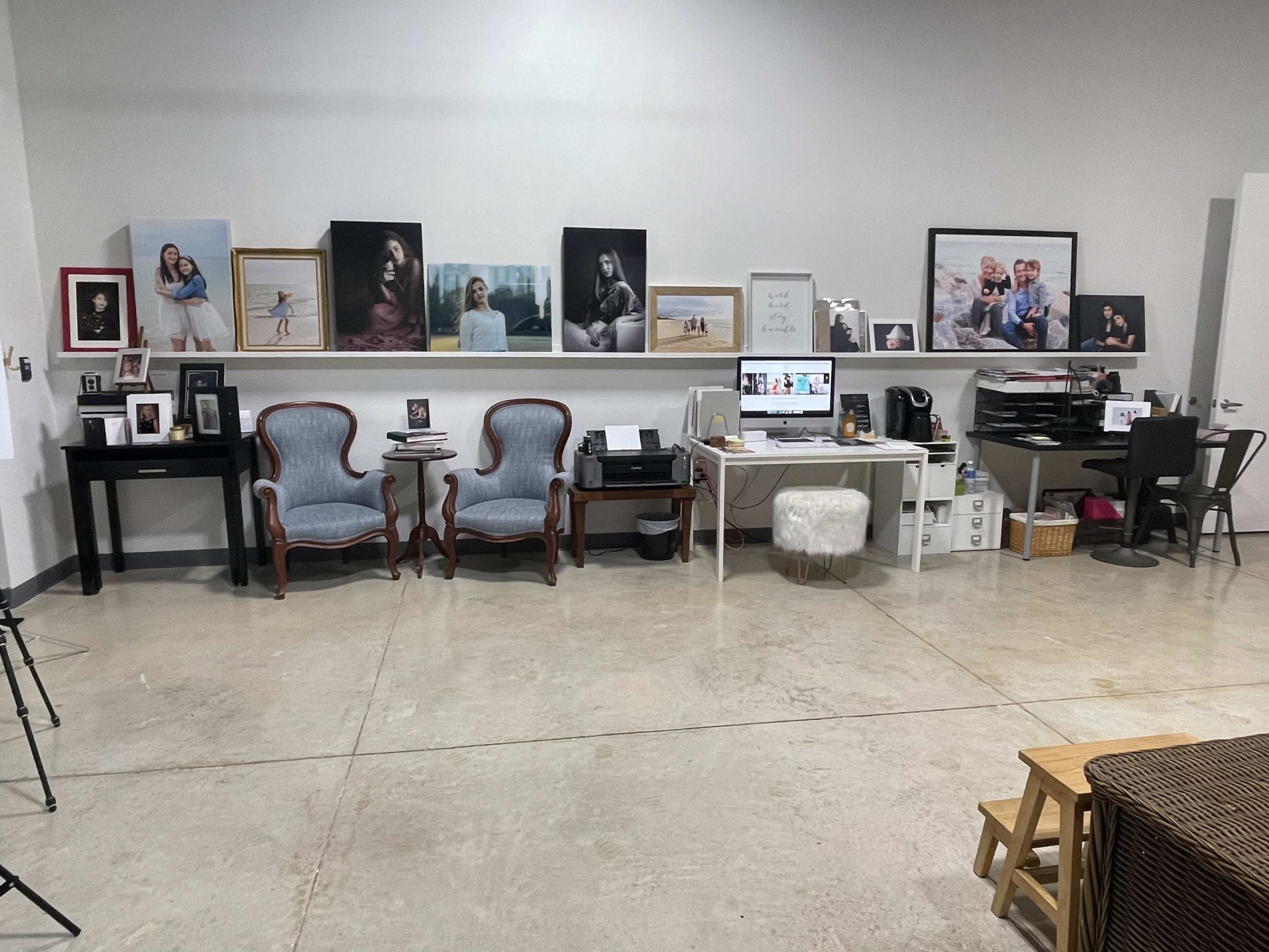 A spacious room with a workspace featuring a desk and computer, several framed photographs on the walls, and two upholstered chairs.