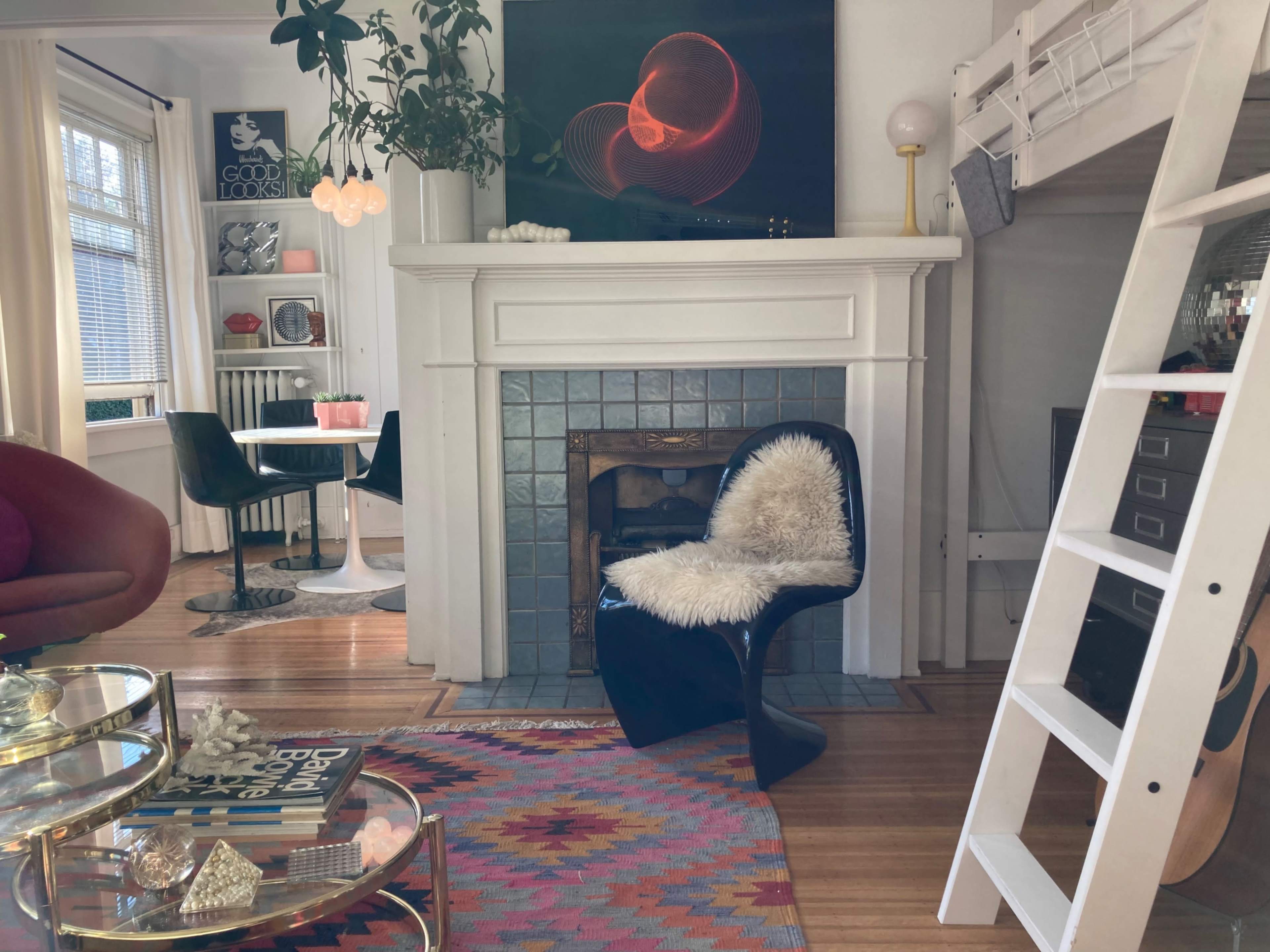 A cozy room featuring a black chair with a furry seat, a white ladder leading to a loft, and a fireplace with decorative items above it.