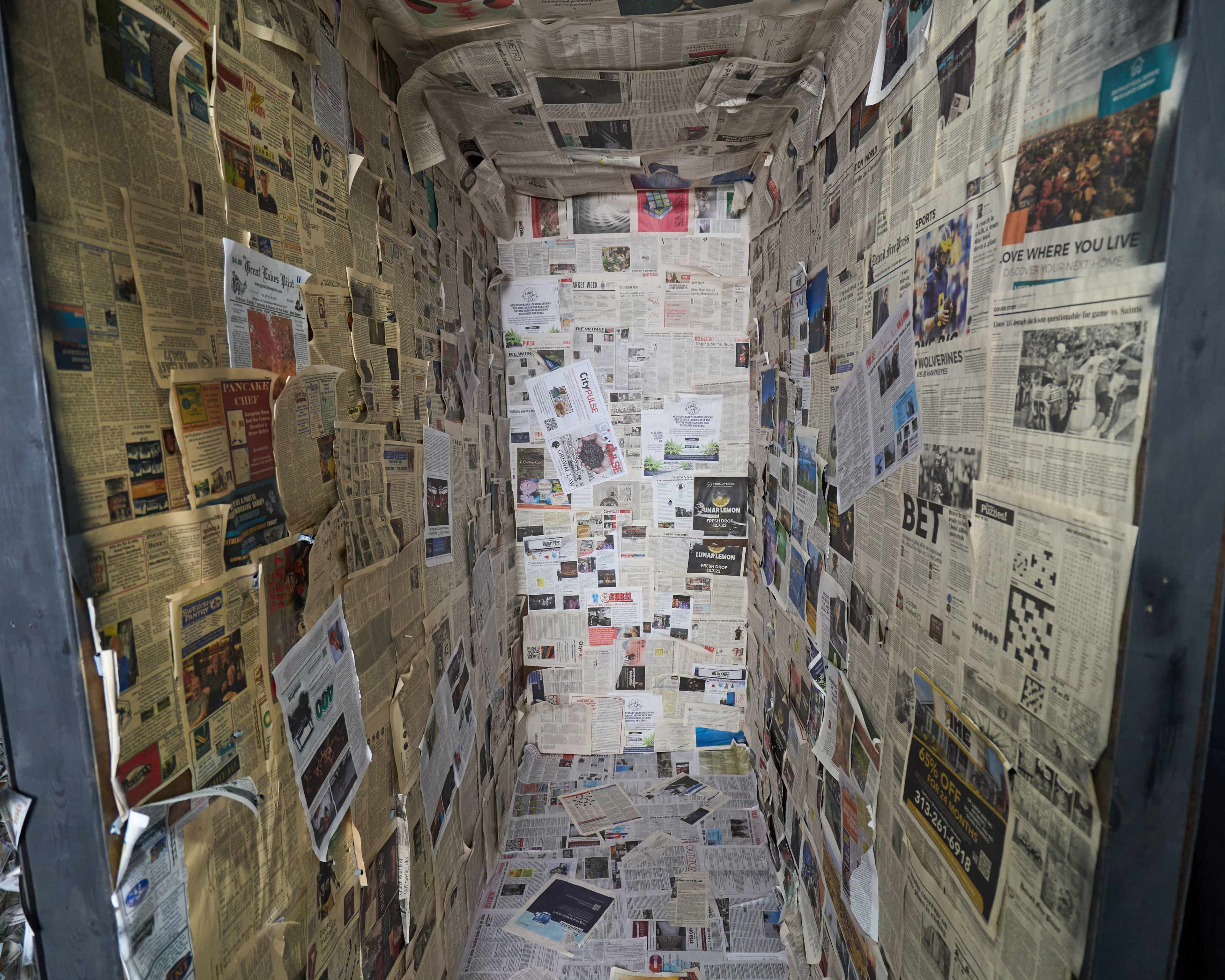 The interior of a small enclosed space is completely covered with various newspaper clippings and articles on all walls.