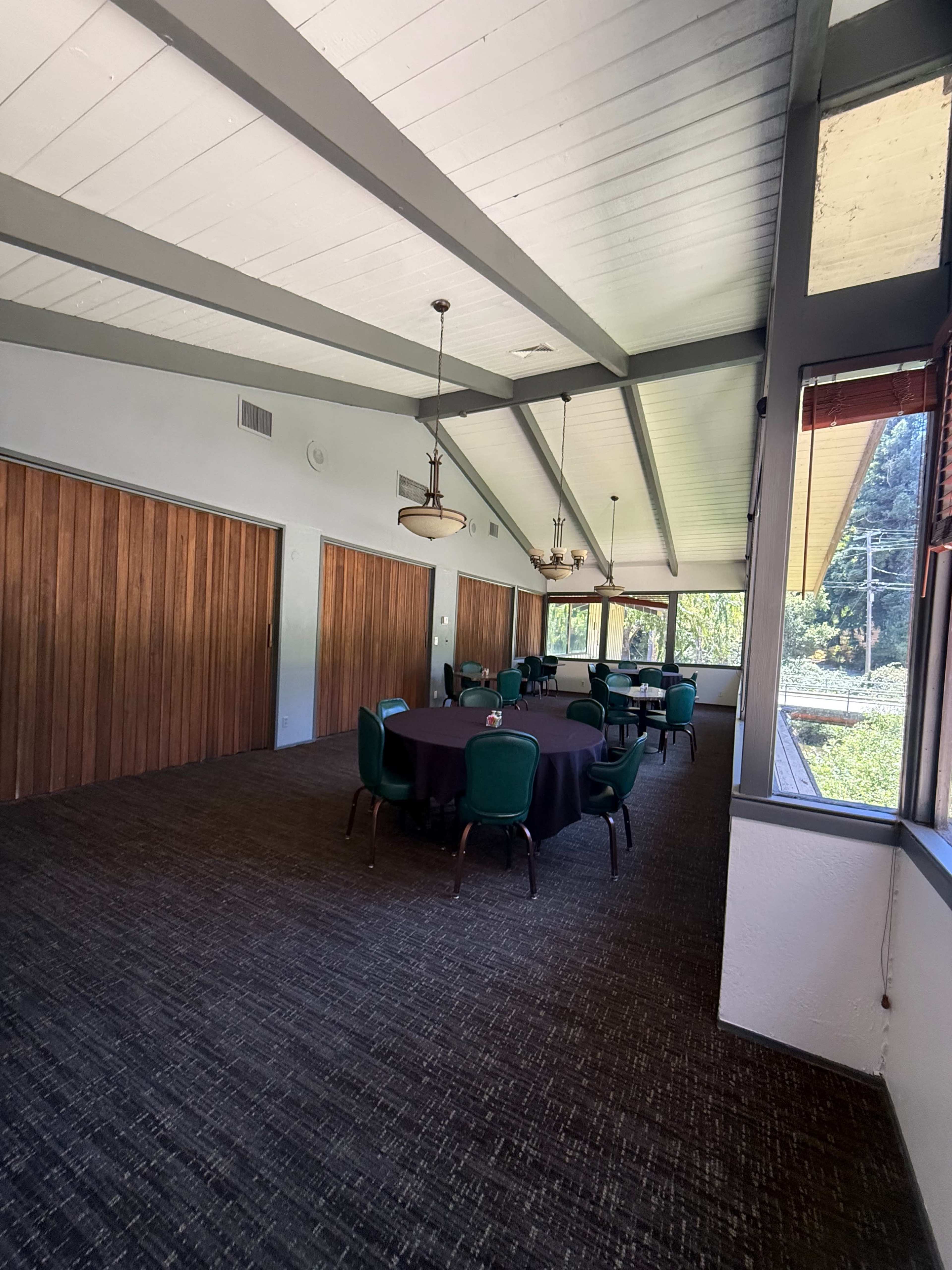 The image shows a large meeting room with a table set for dining, surrounded by green chairs and wooden sliding doors along one wall.