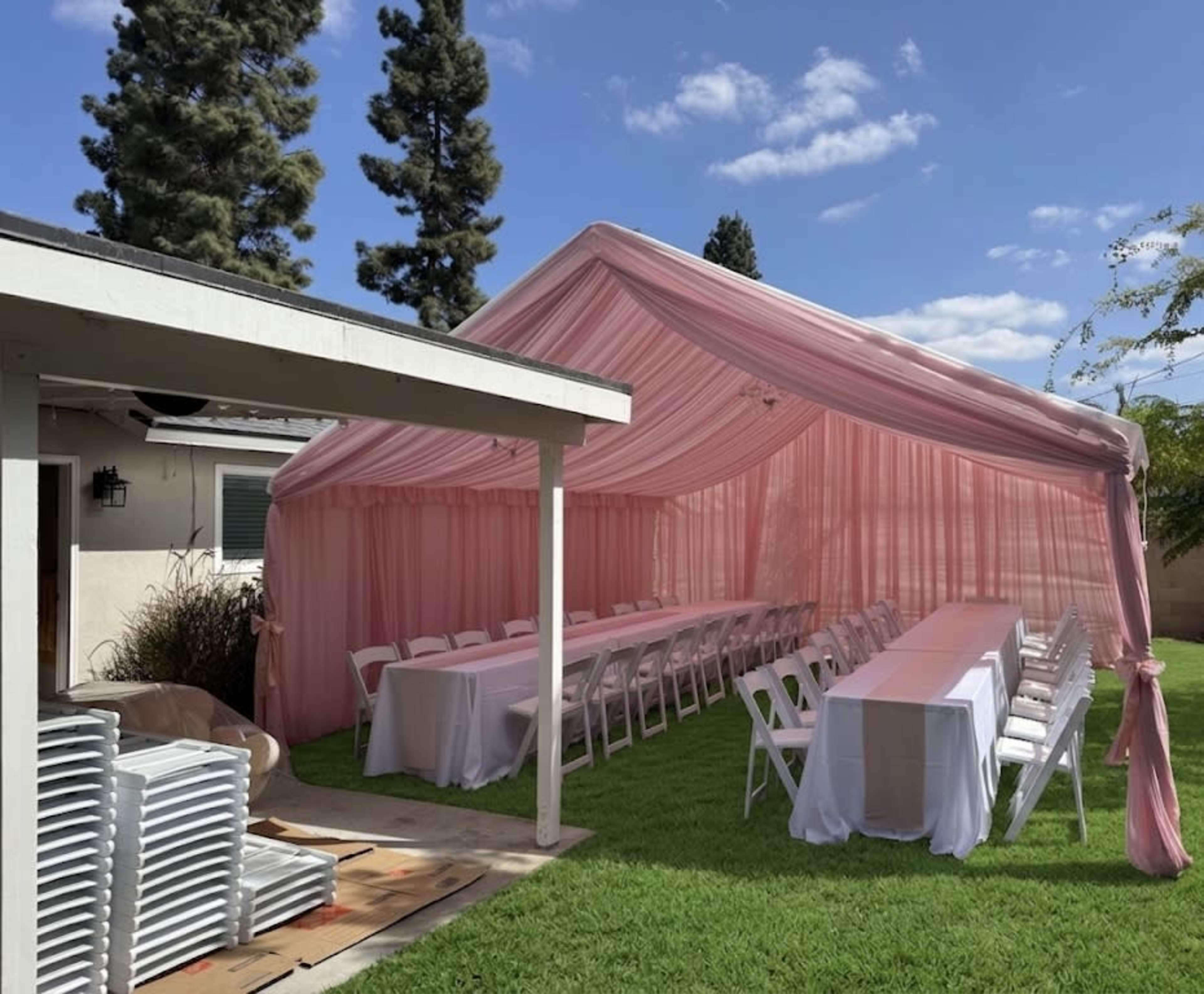A large pink tent with white tables and chairs is set up on a green lawn beside a building.
