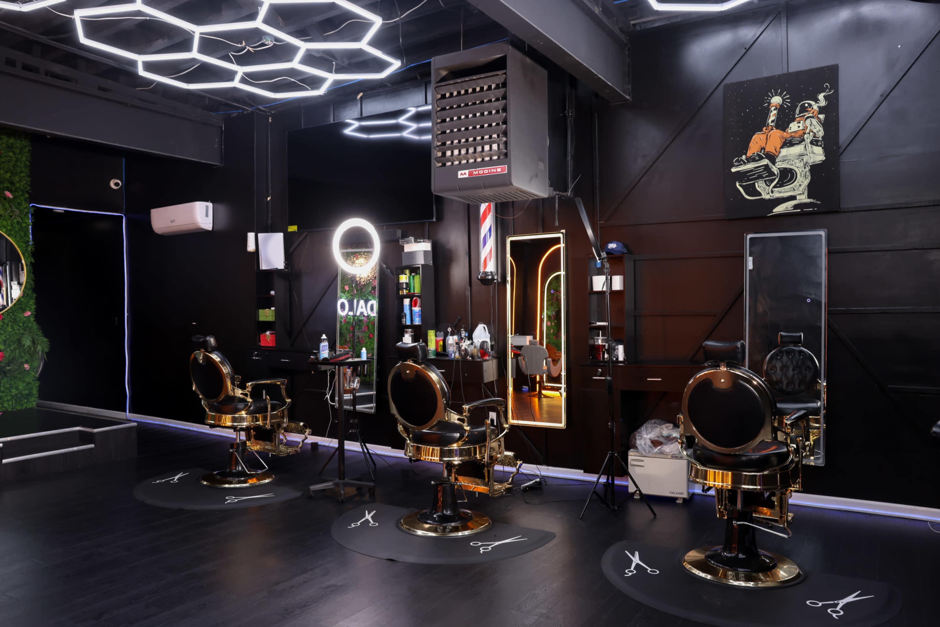 The image shows a sleek barber shop interior with three black and gold barber chairs, illuminated by modern lighting and decorated with grooming tools and mirrors.