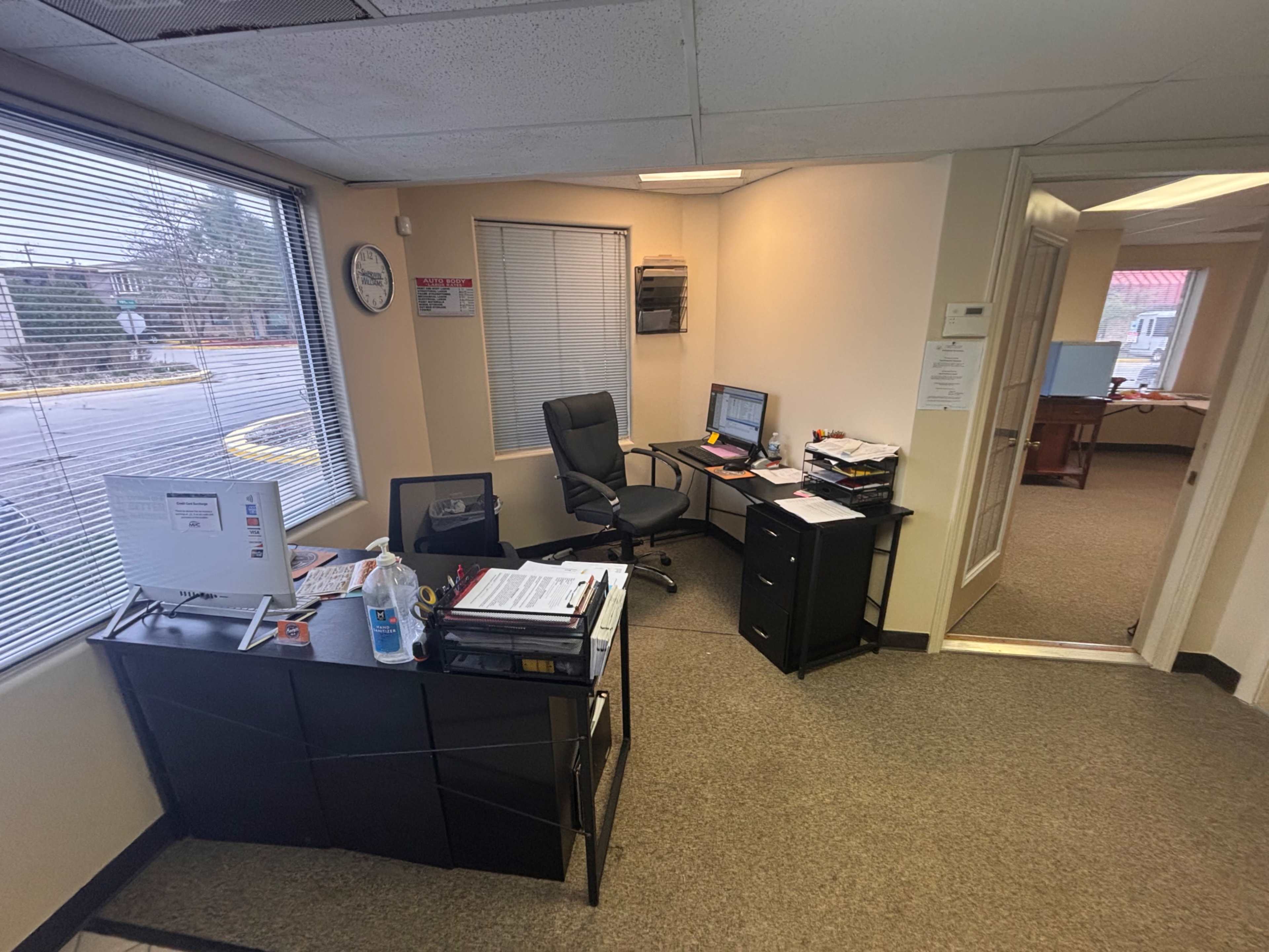 The image shows an office space with a desk, chair, computer, and large windows allowing natural light to enter.