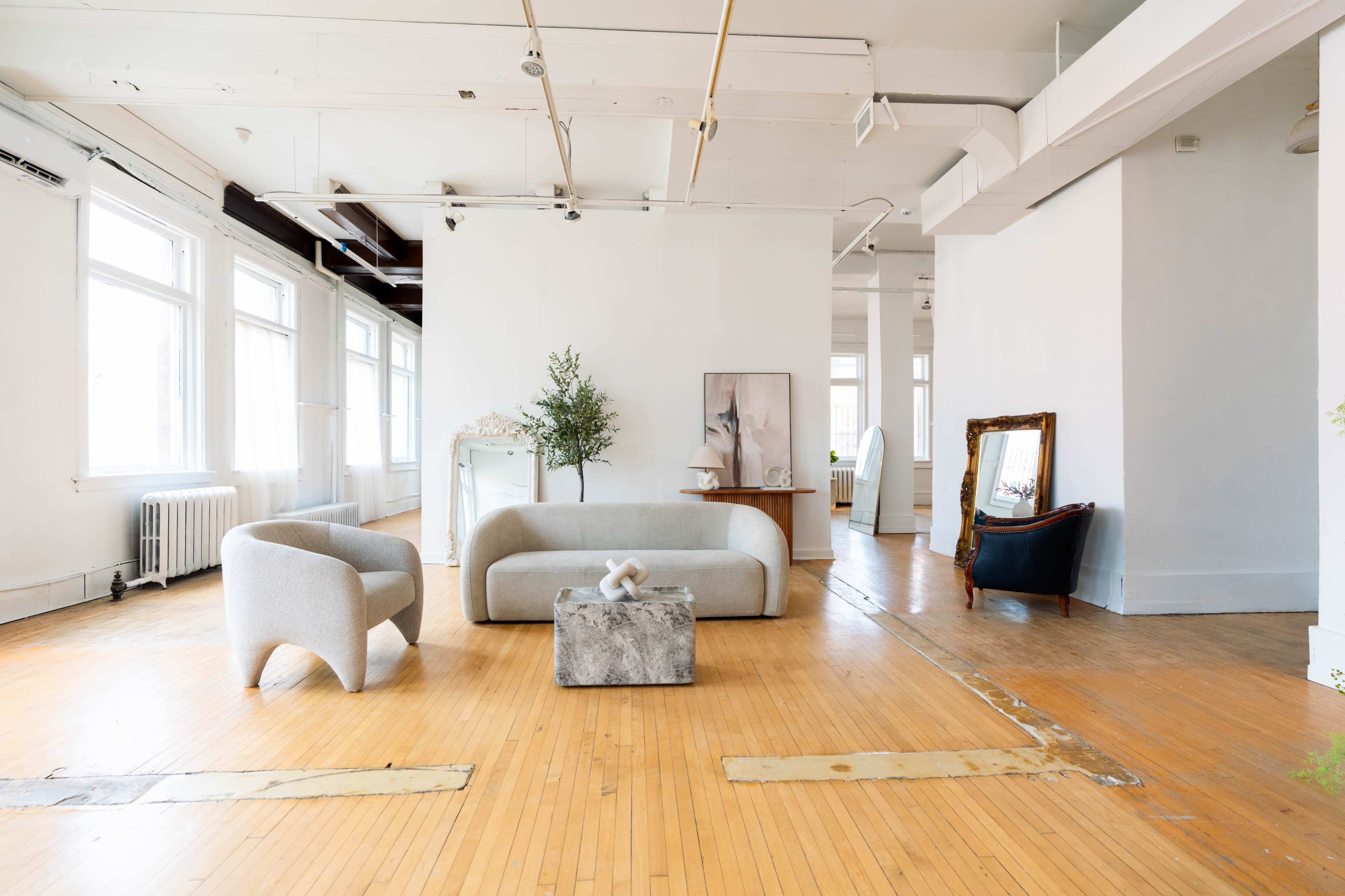 The room features two modern sofas and a concrete coffee table on a wooden floor, with large windows allowing natural light to fill the space.