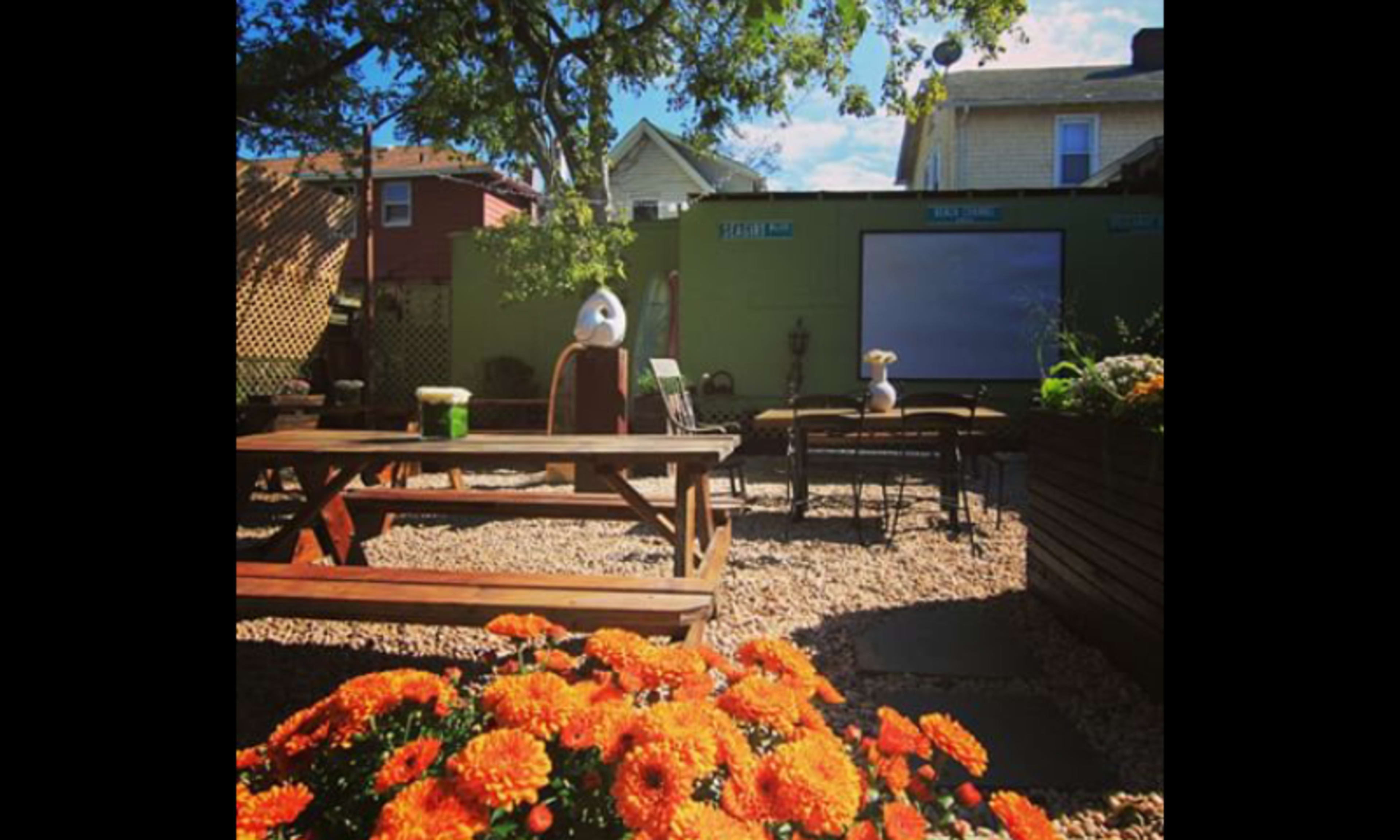 A backyard seating area with a wooden picnic table, several chairs, and vibrant orange flowers in the foreground.