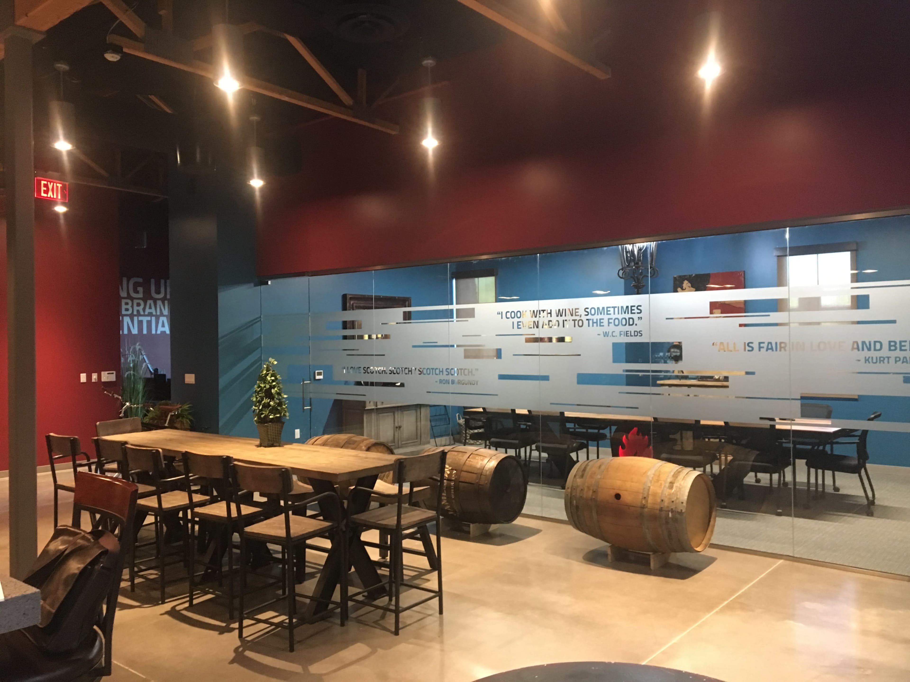 A modern dining area features wooden tables and chairs, with a large glass wall displaying a motivational quote and decorative elements.