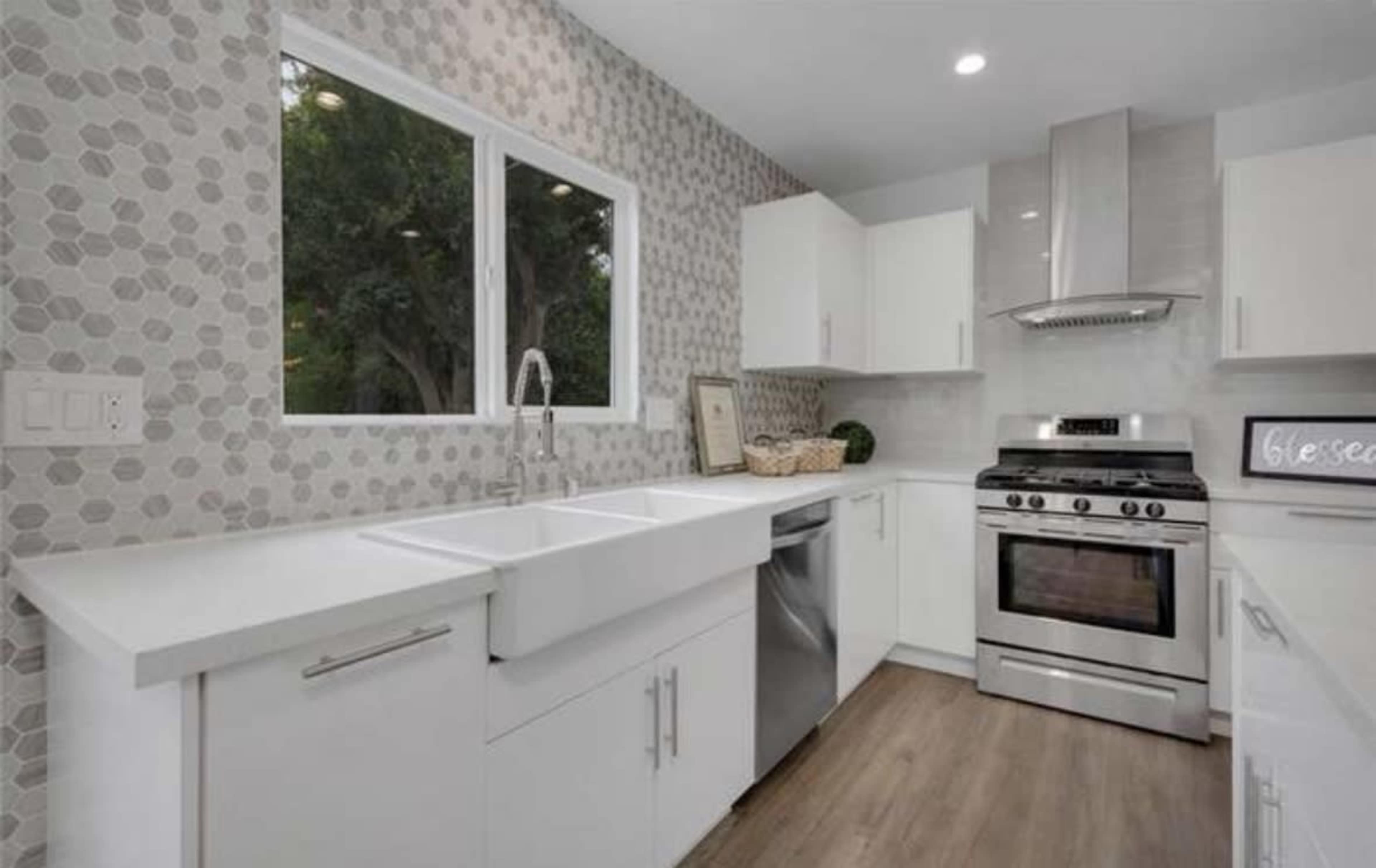A modern kitchen featuring a farmhouse sink, stainless steel appliances, and geometric tile accents on the walls.